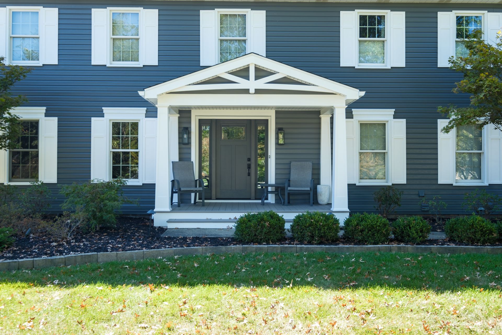 Blue house with white trim and front porch, two chairs, green lawn.
