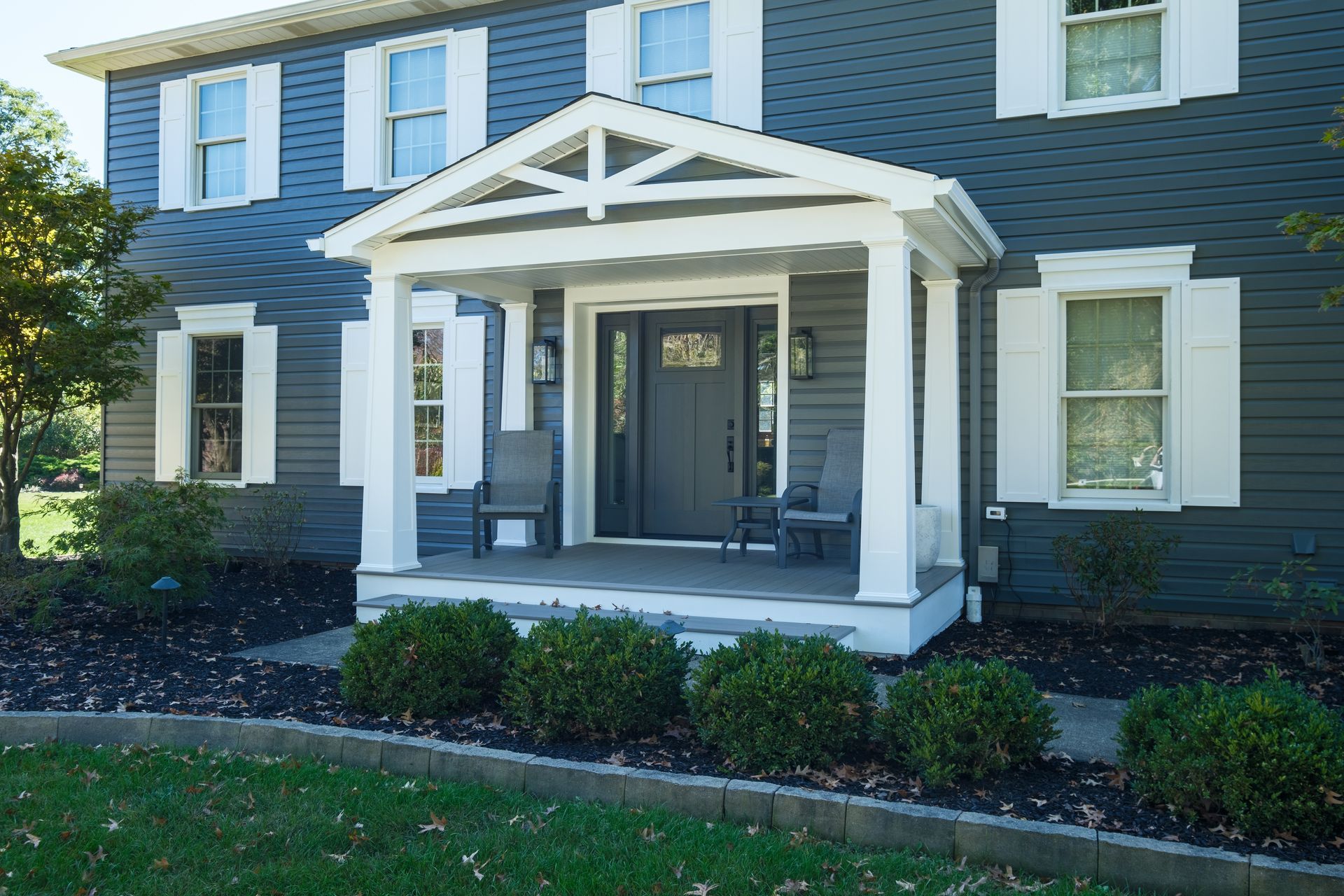 Gray house with white trim, front porch, and shutters, with landscaping.