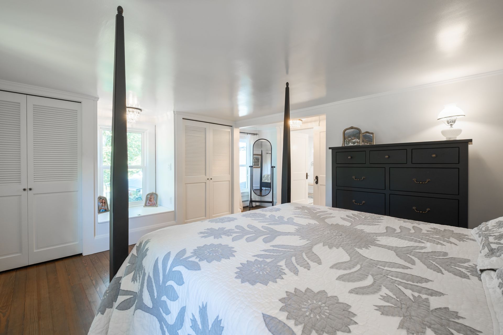 Bedroom with four-poster bed, white walls, dark dresser and closet doors.