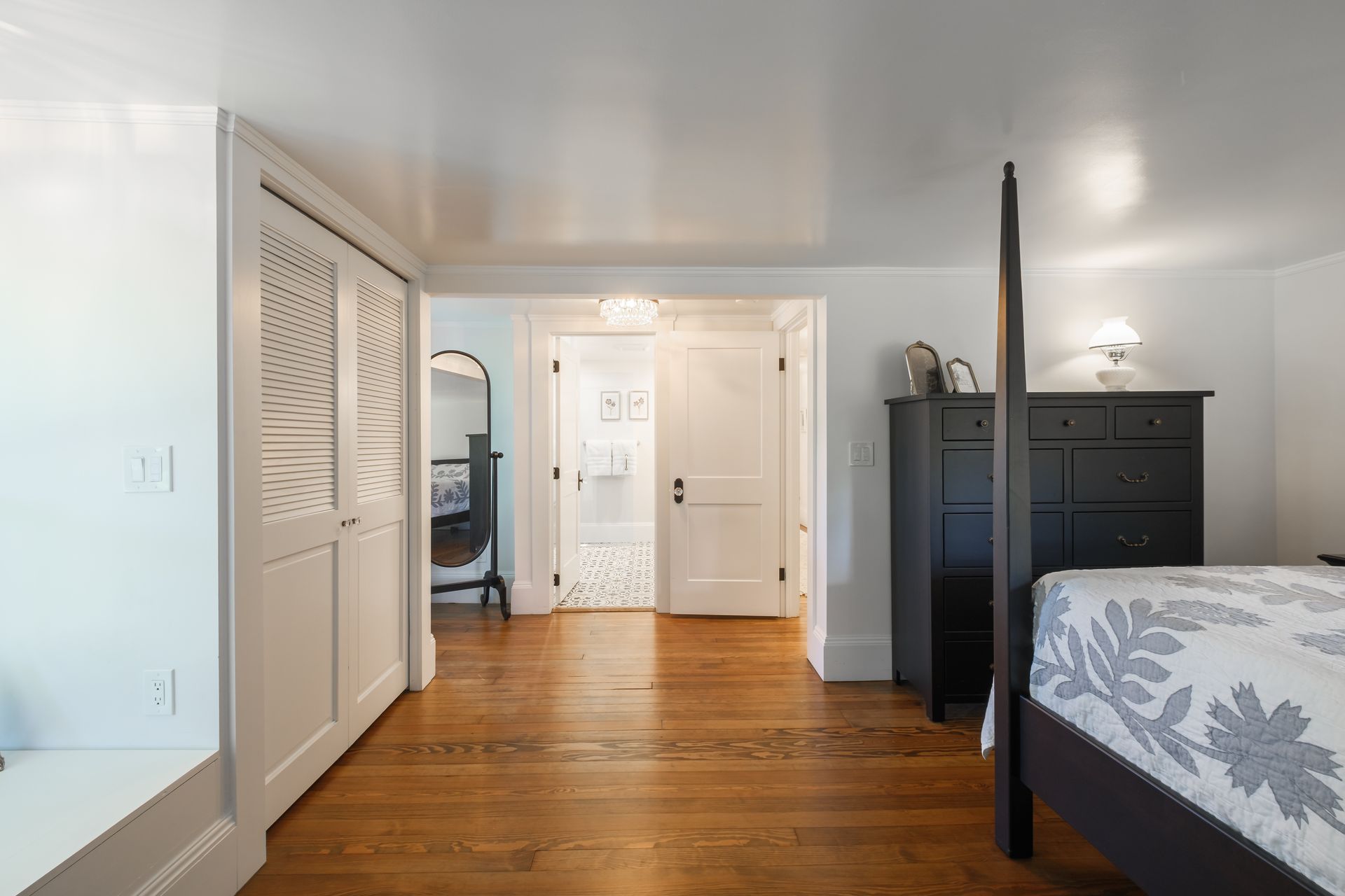 Bedroom with wood floors, white walls, black dresser, and a door leading to a bathroom.