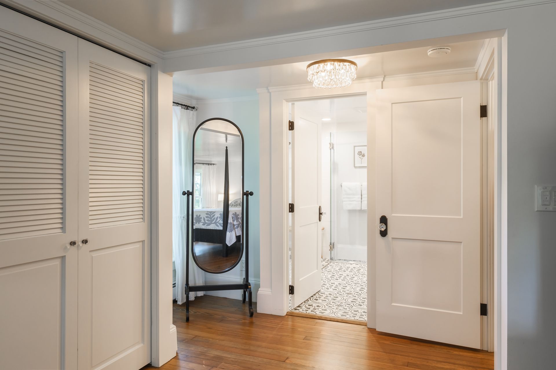 White hallway with closet doors, a mirror, and open doors leading to a bathroom.