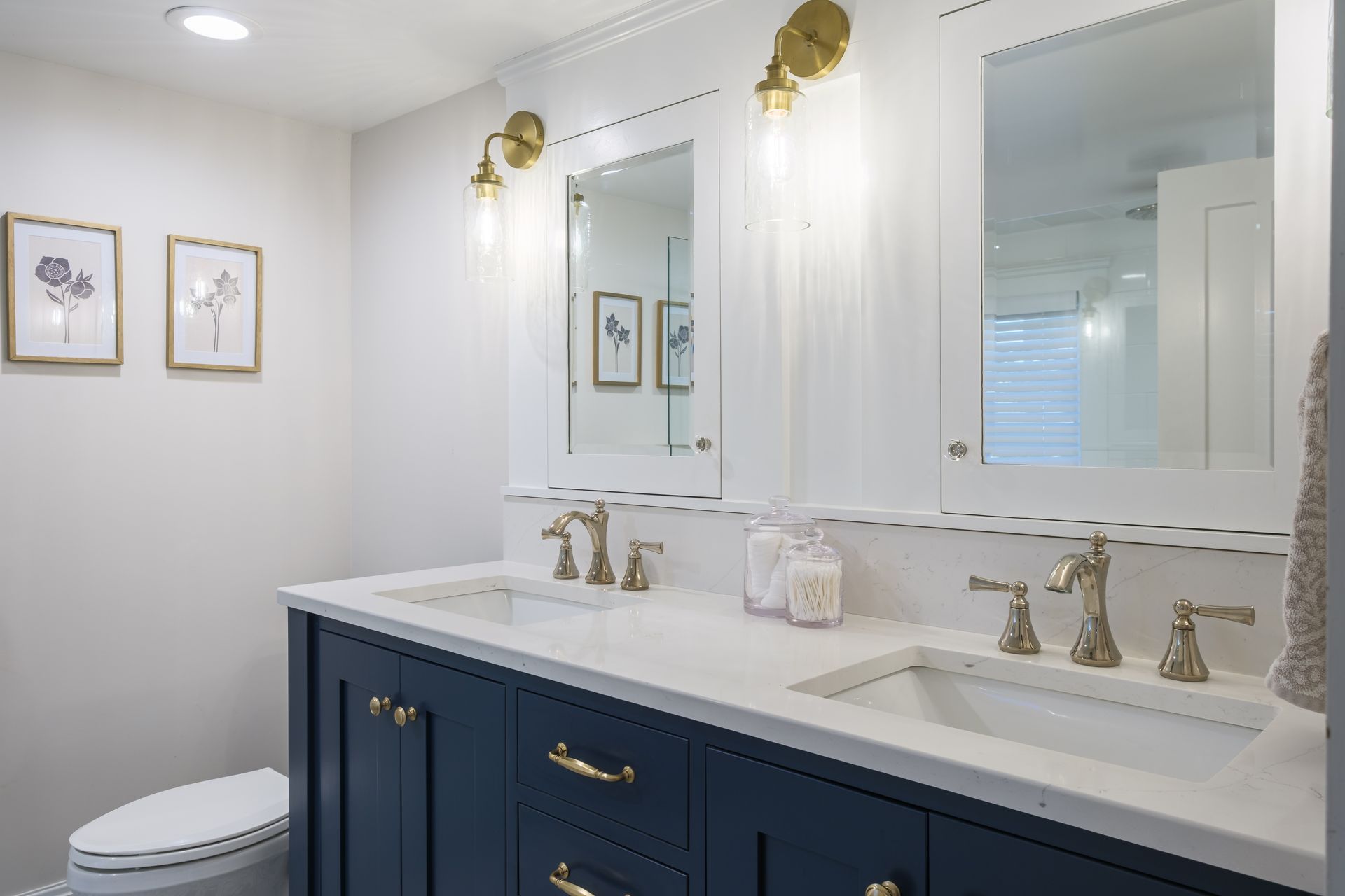 Bathroom with navy blue vanity, white countertop, gold fixtures, and framed artwork.