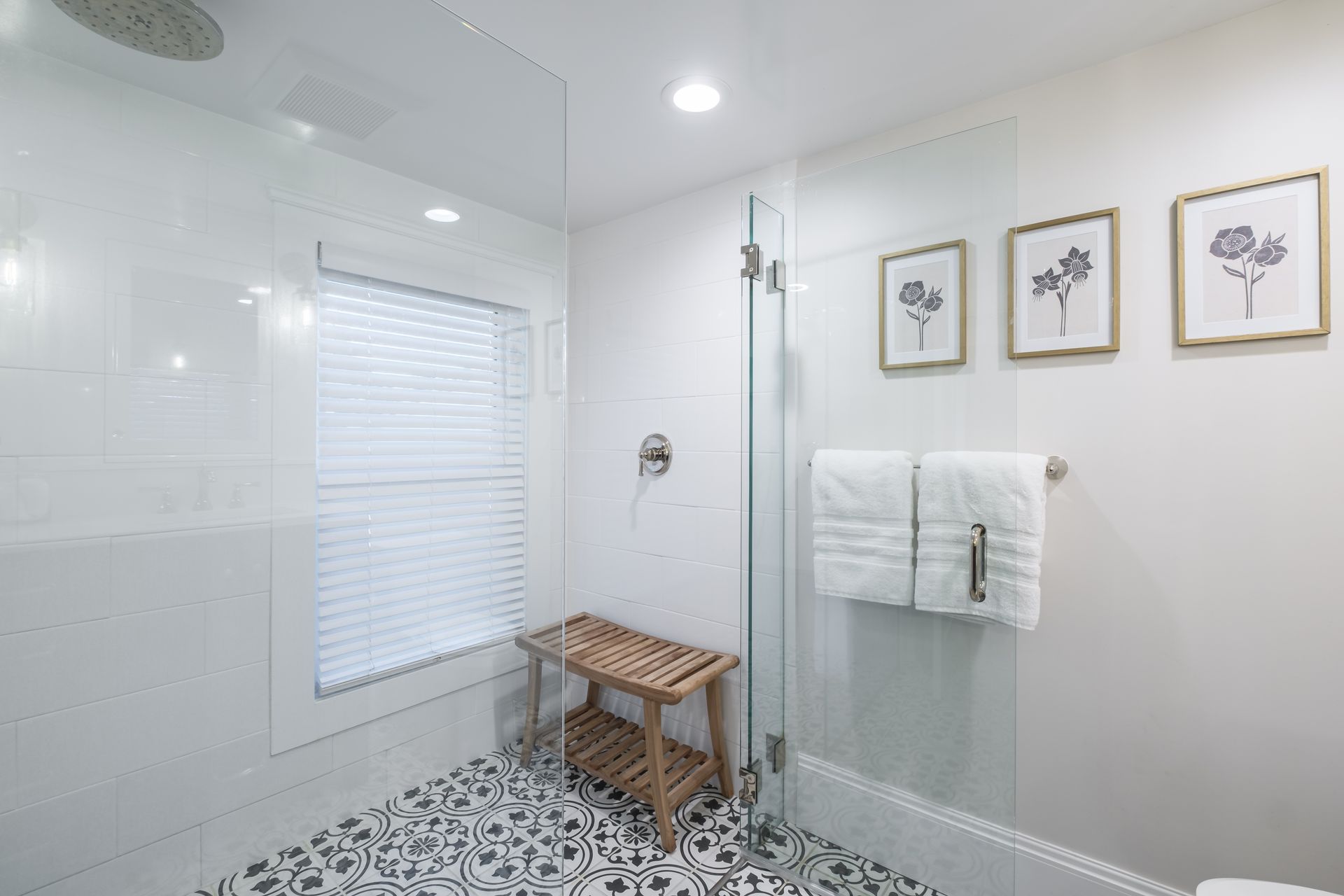 Modern white bathroom with a glass shower, floral artwork, and a wooden bench.