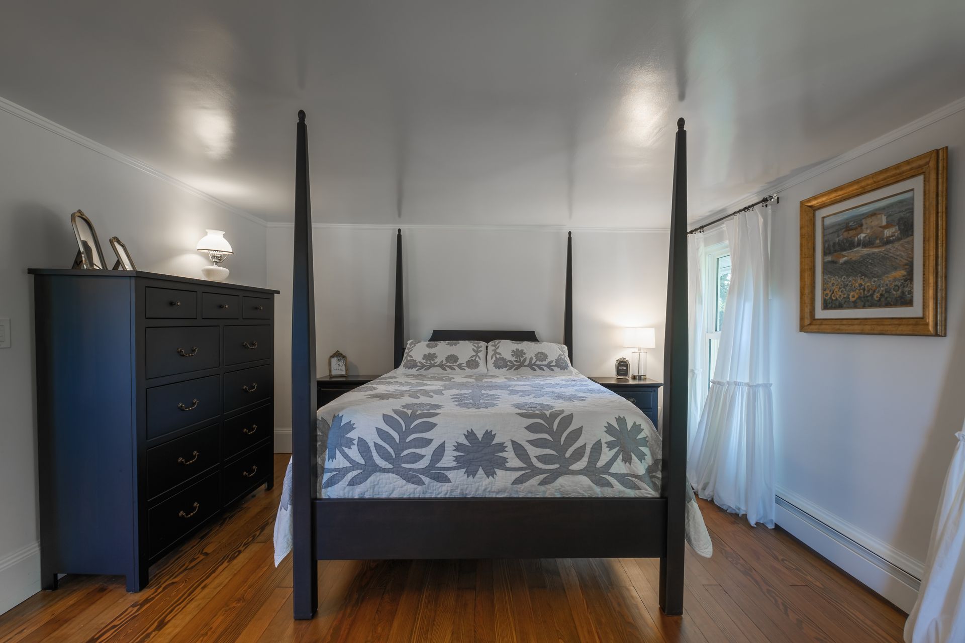 Bedroom with black four-poster bed, dresser, nightstands, and artwork on a wooden floor.