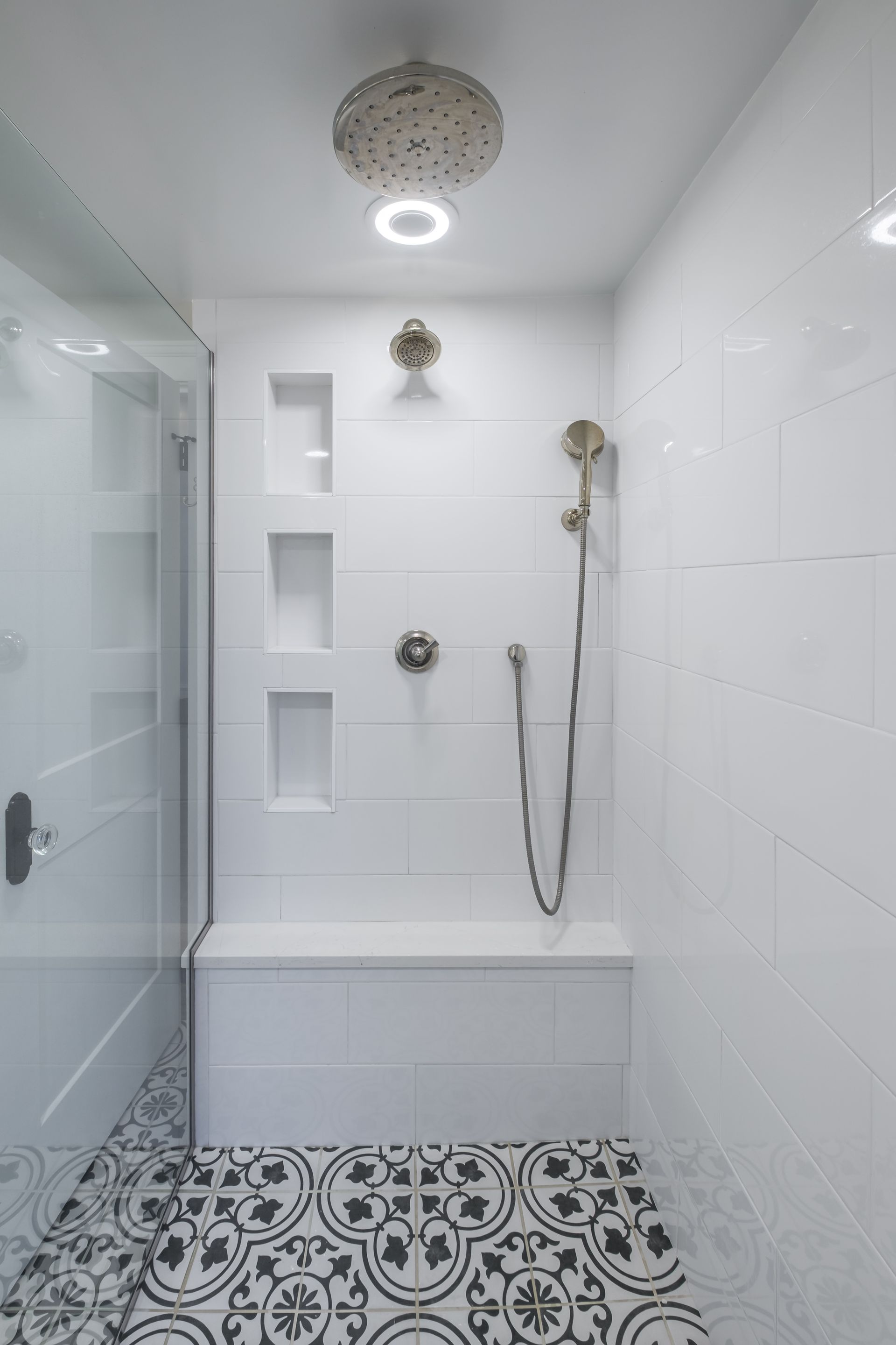 White tiled shower with glass door, bench, and patterned floor.