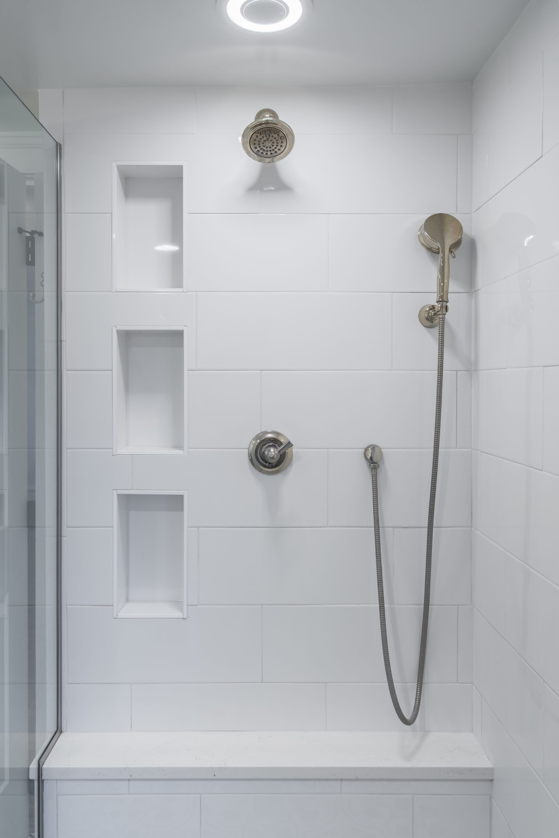 White-tiled shower with built-in shelves, gold fixtures, and a bench.