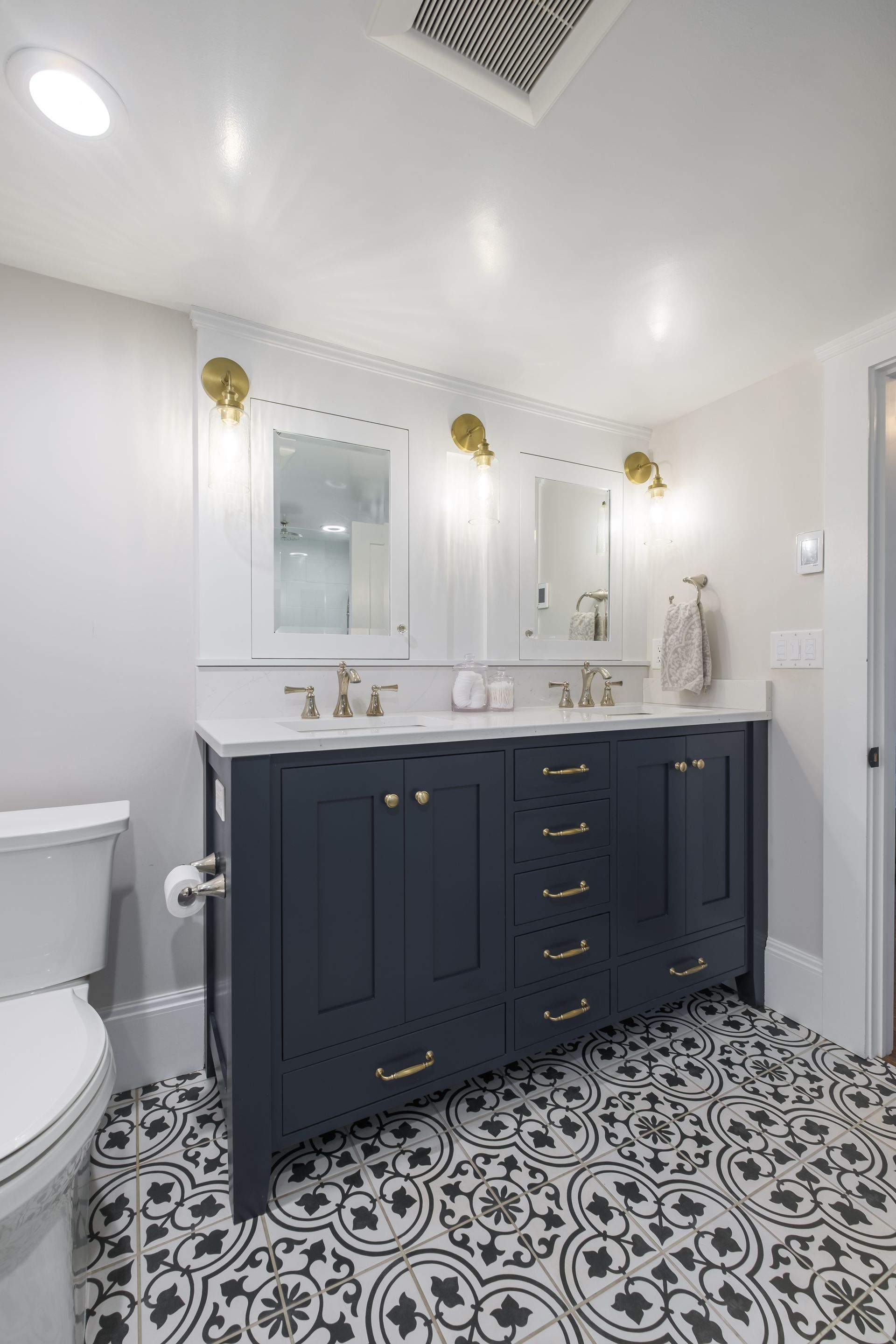 Bathroom with navy blue vanity, white marble countertop, patterned tile floor, and gold accents.