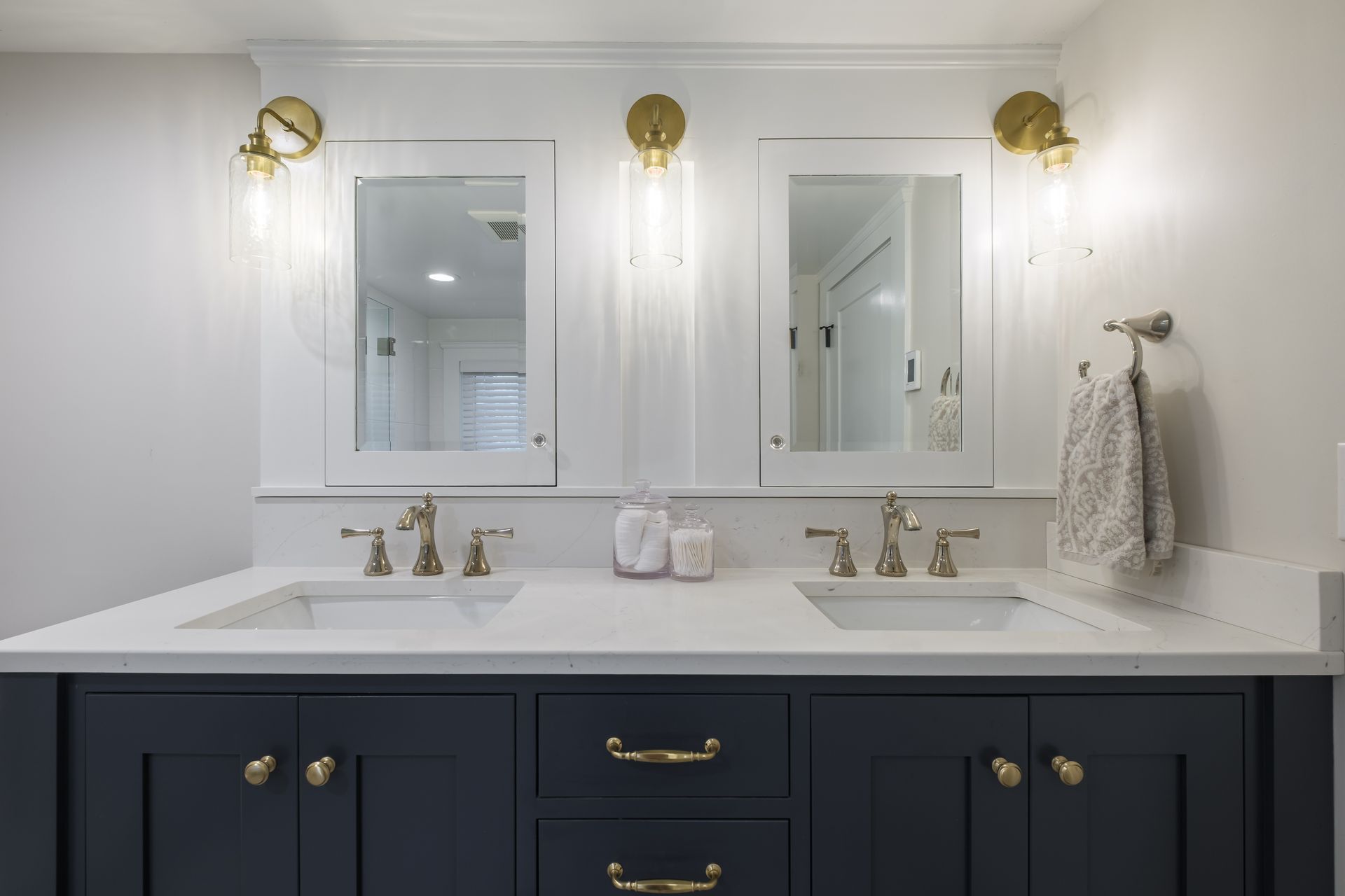 Bathroom vanity with blue cabinets, white countertop, gold fixtures, and two mirrors.