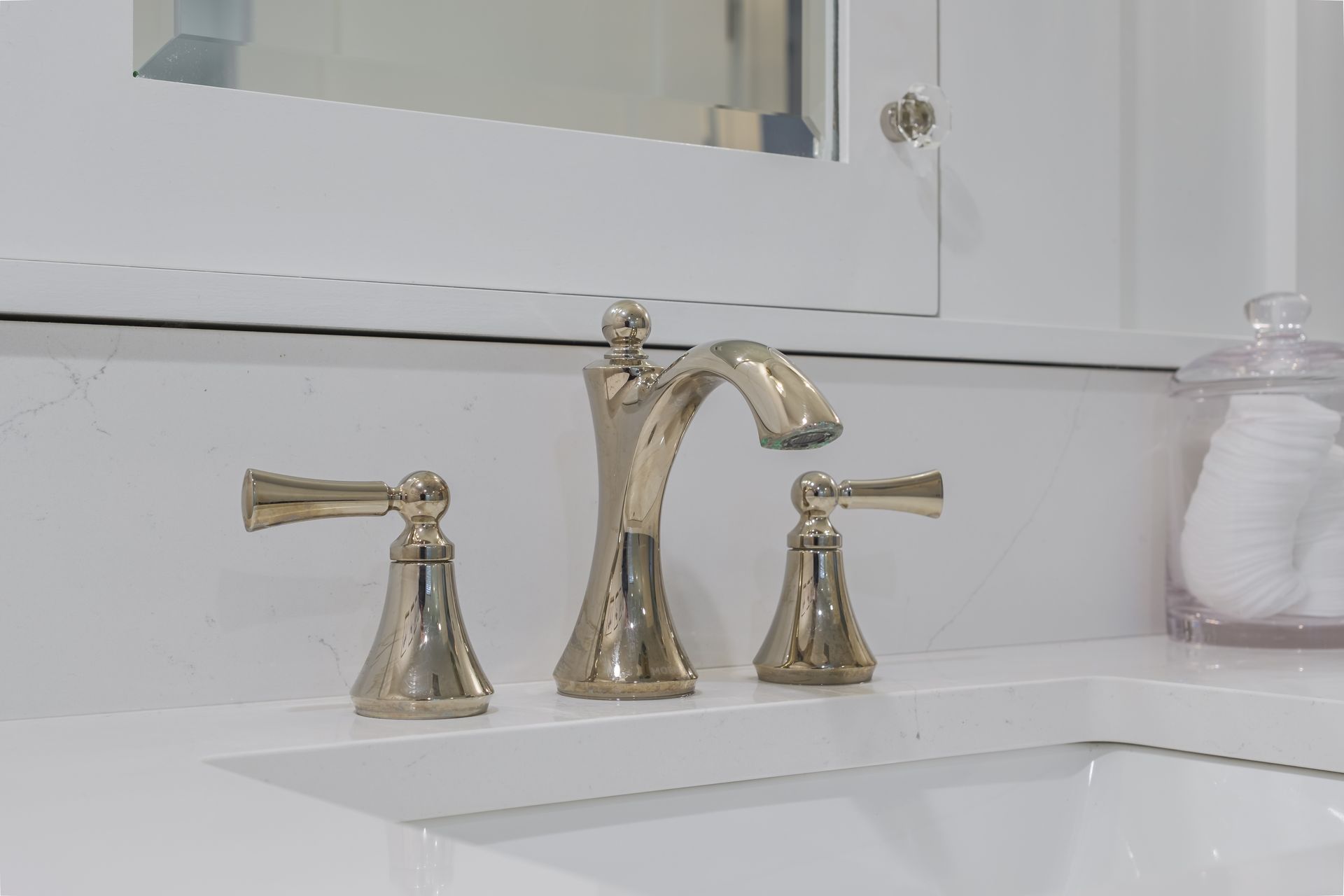 Gold bathroom faucet with two handles on a white countertop.