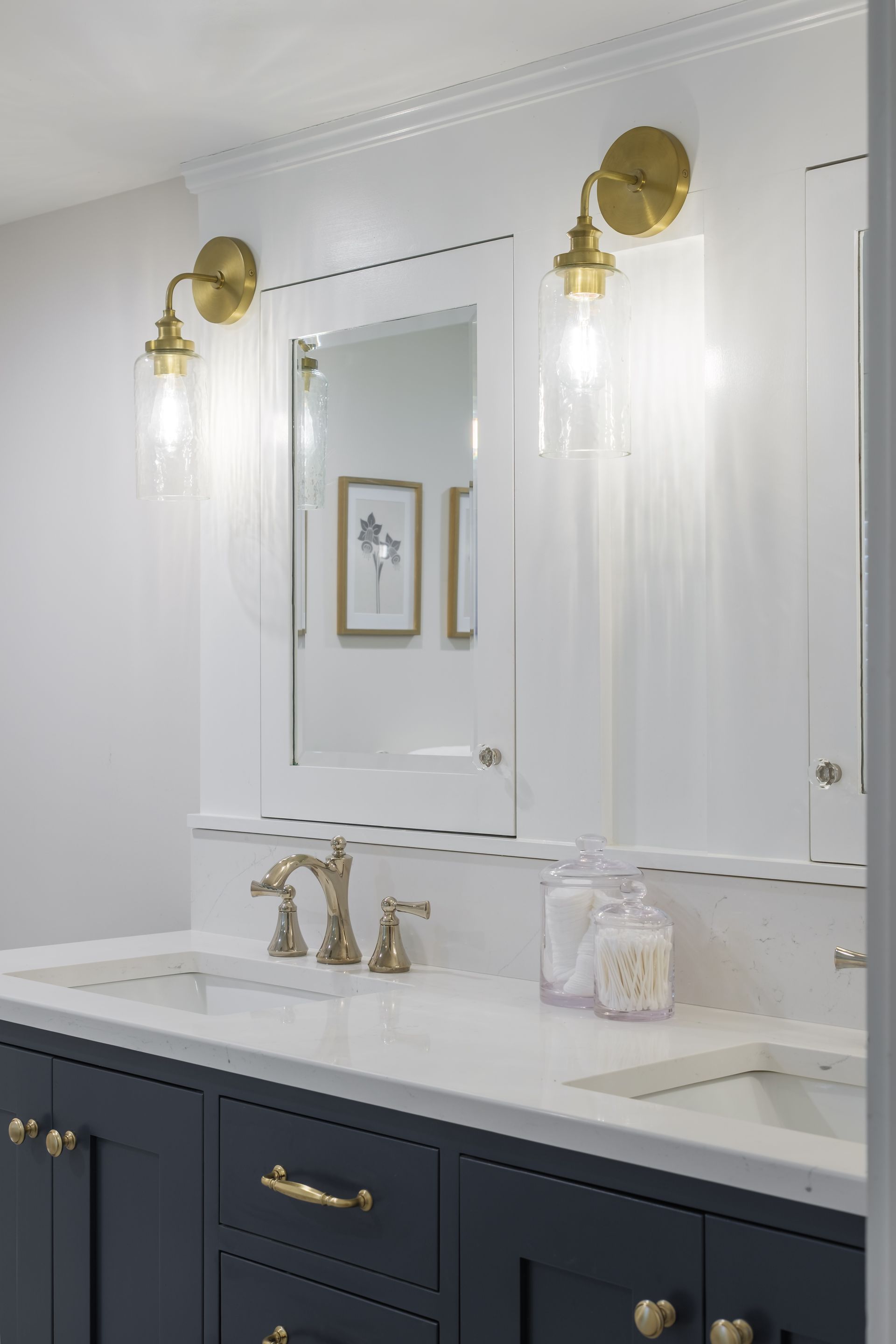 Bathroom with a dark blue vanity, white countertop, gold fixtures, and sconces.