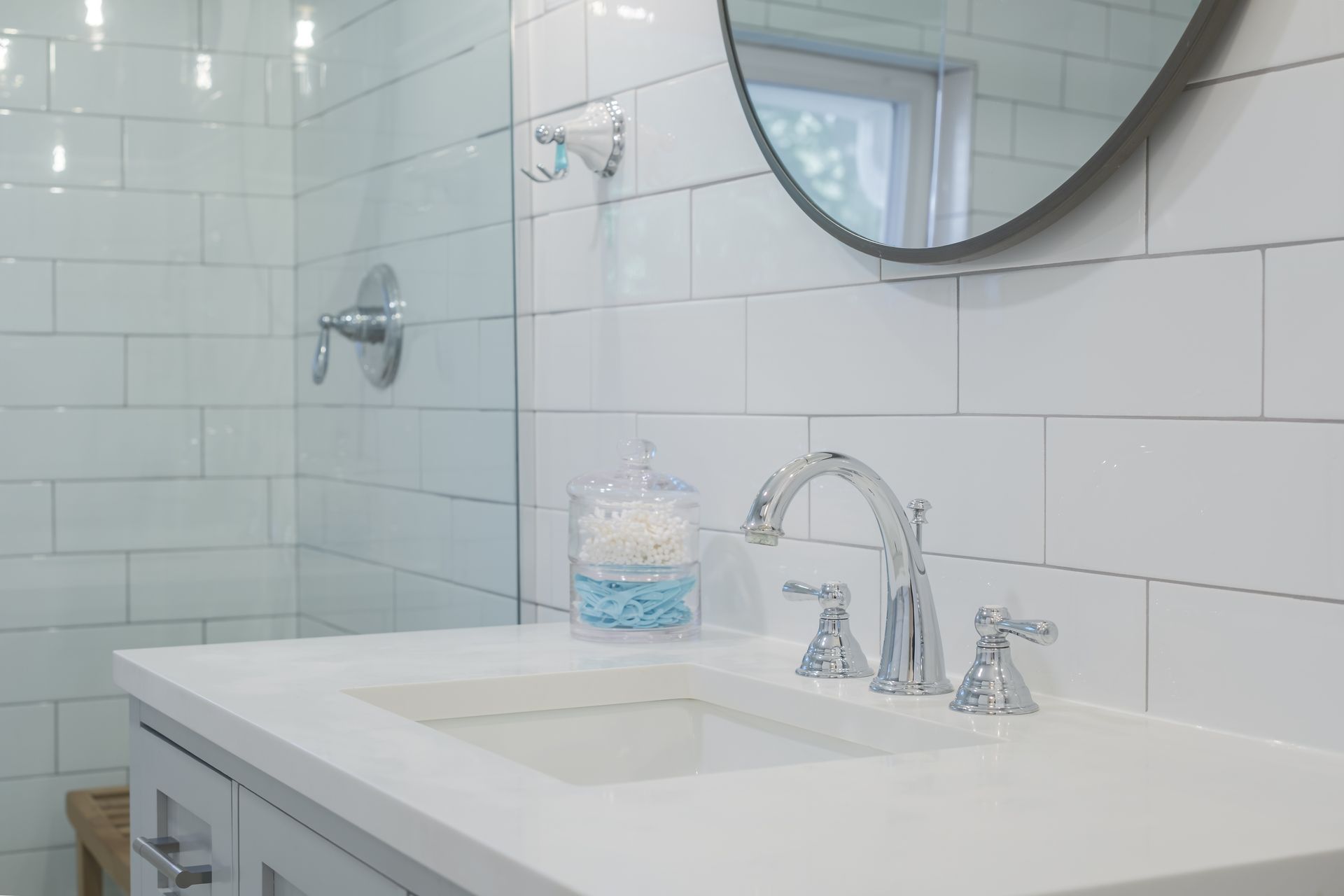 White bathroom with a sink, shower, and round mirror.