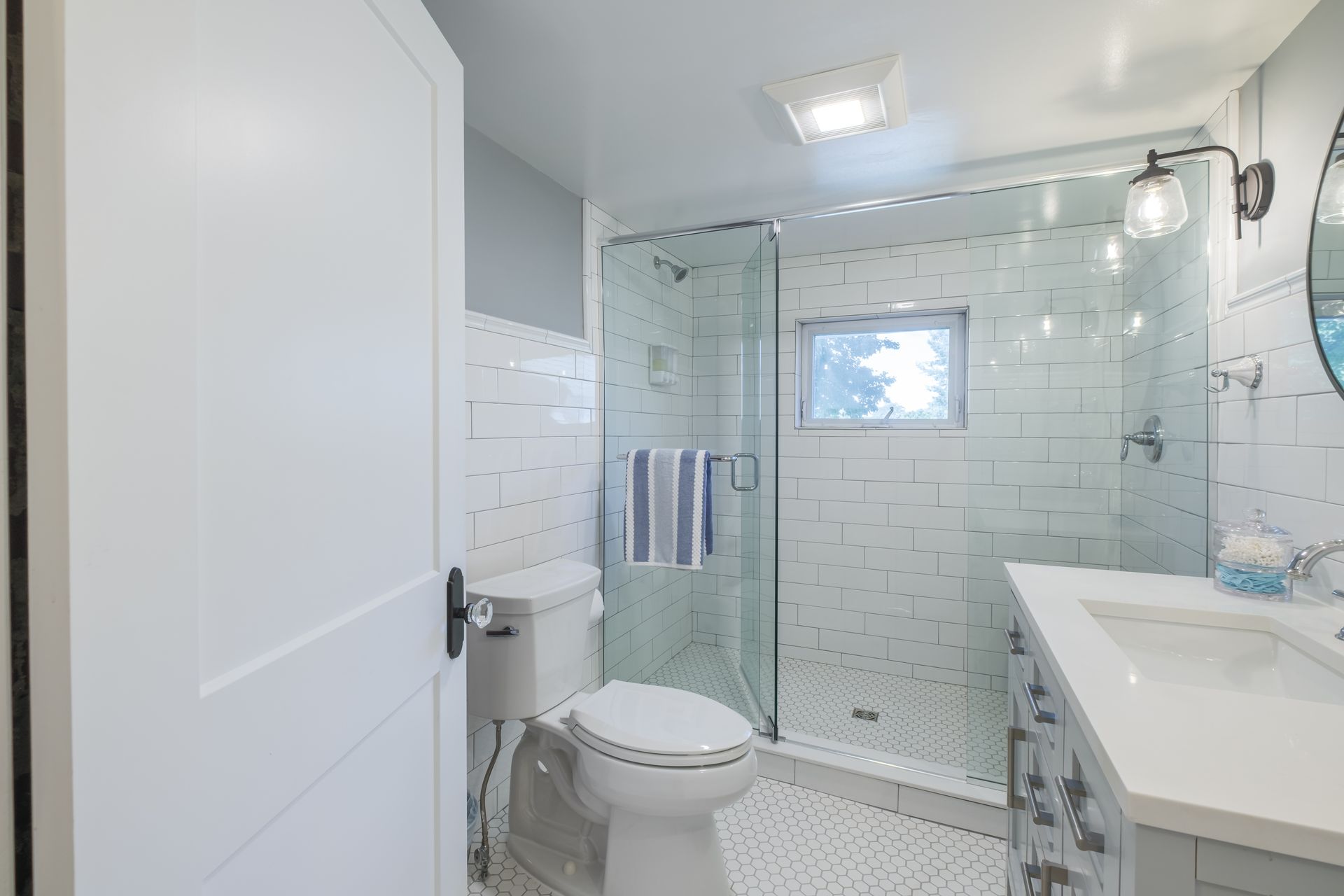 White bathroom with a glass shower, toilet, vanity, and white subway tile.