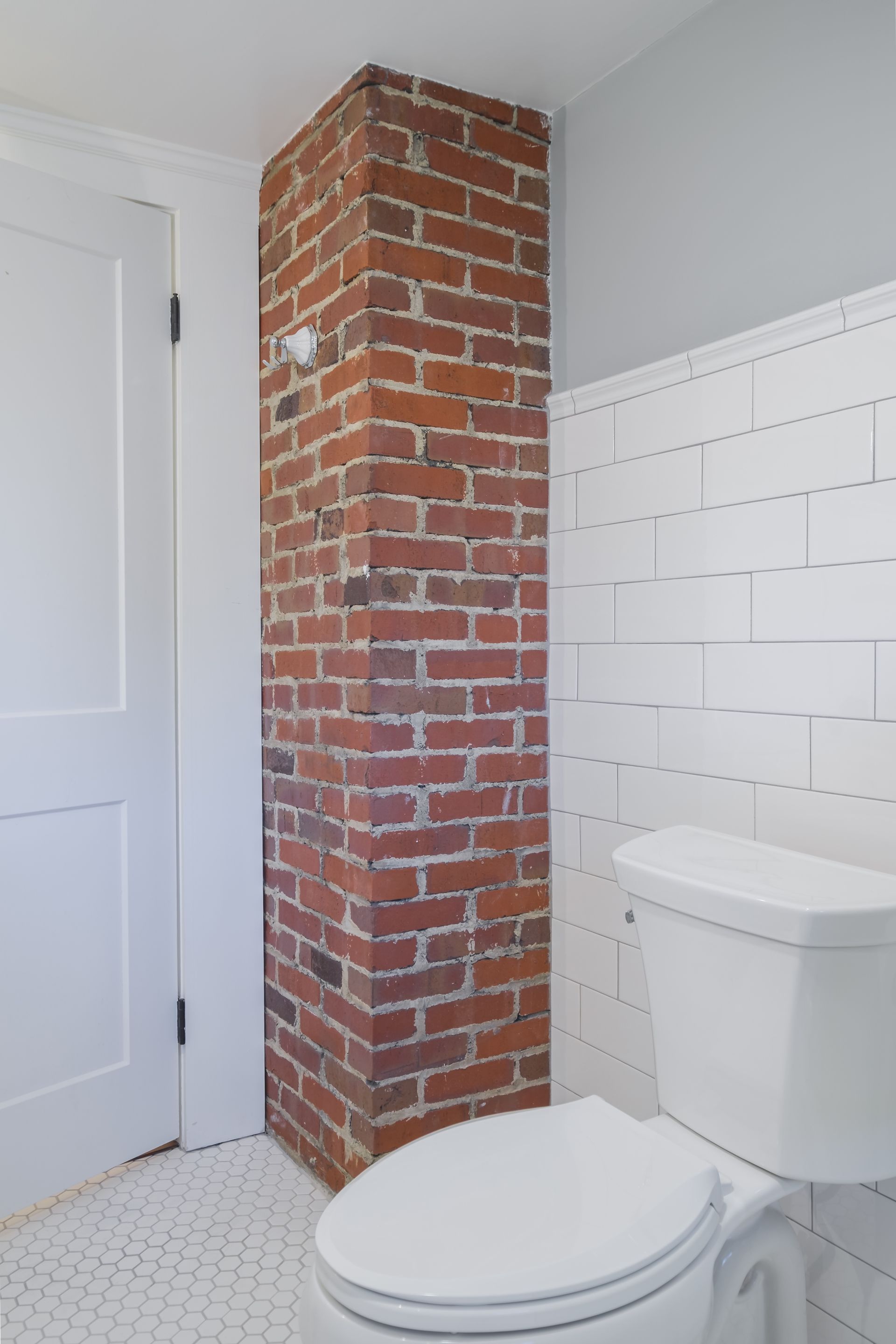 A bathroom with a brick column, white toilet, door, and subway tile wall.