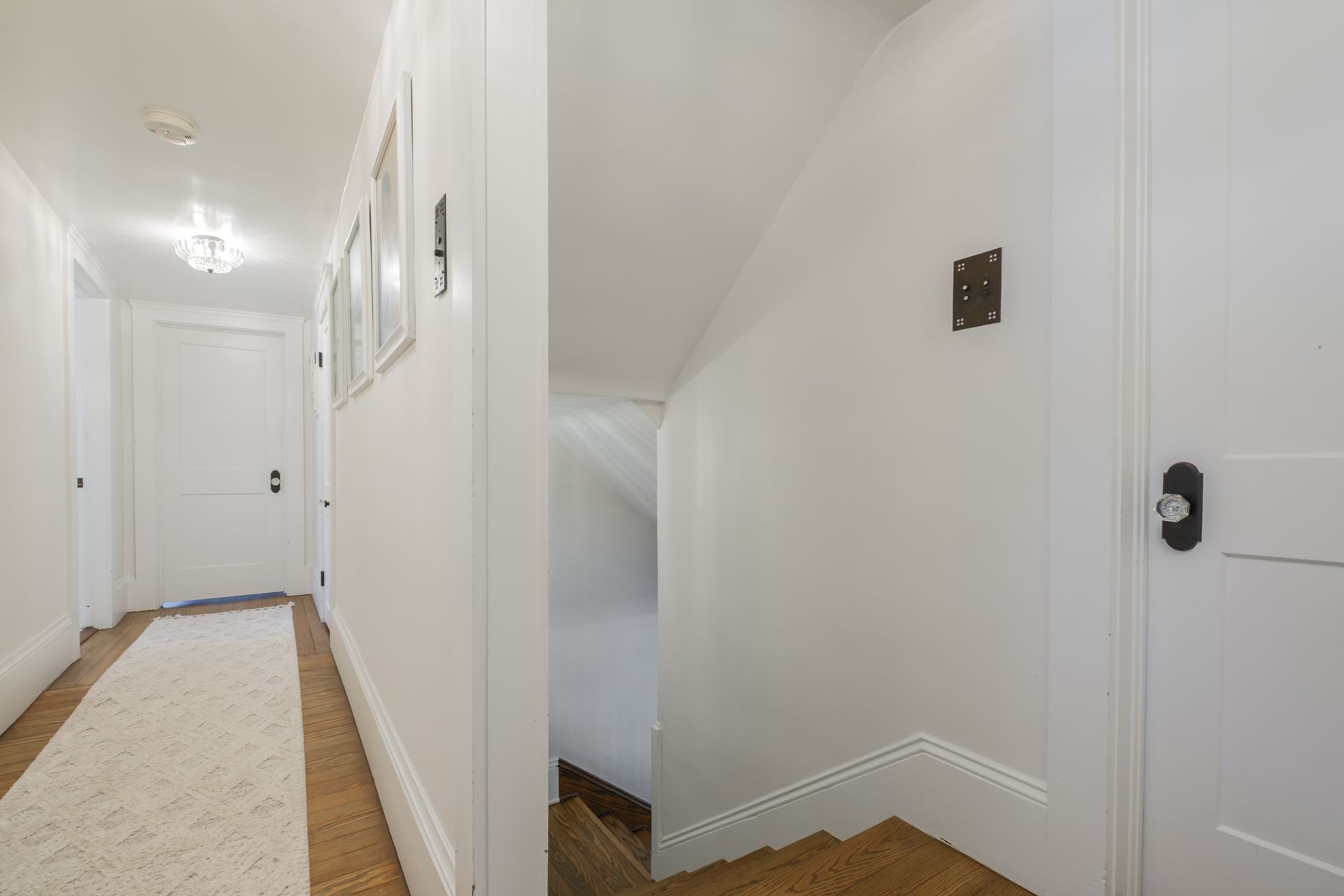 White hallway with closed doors, rug, and staircase with wooden steps.