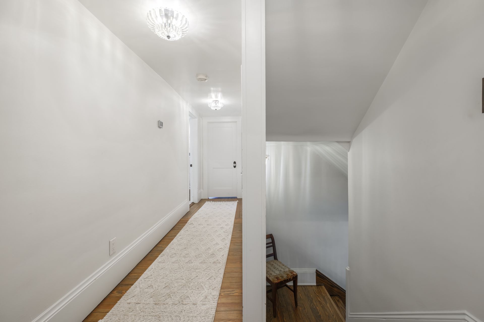 Narrow, white hallway with rug, leading to a closed door and a staircase.