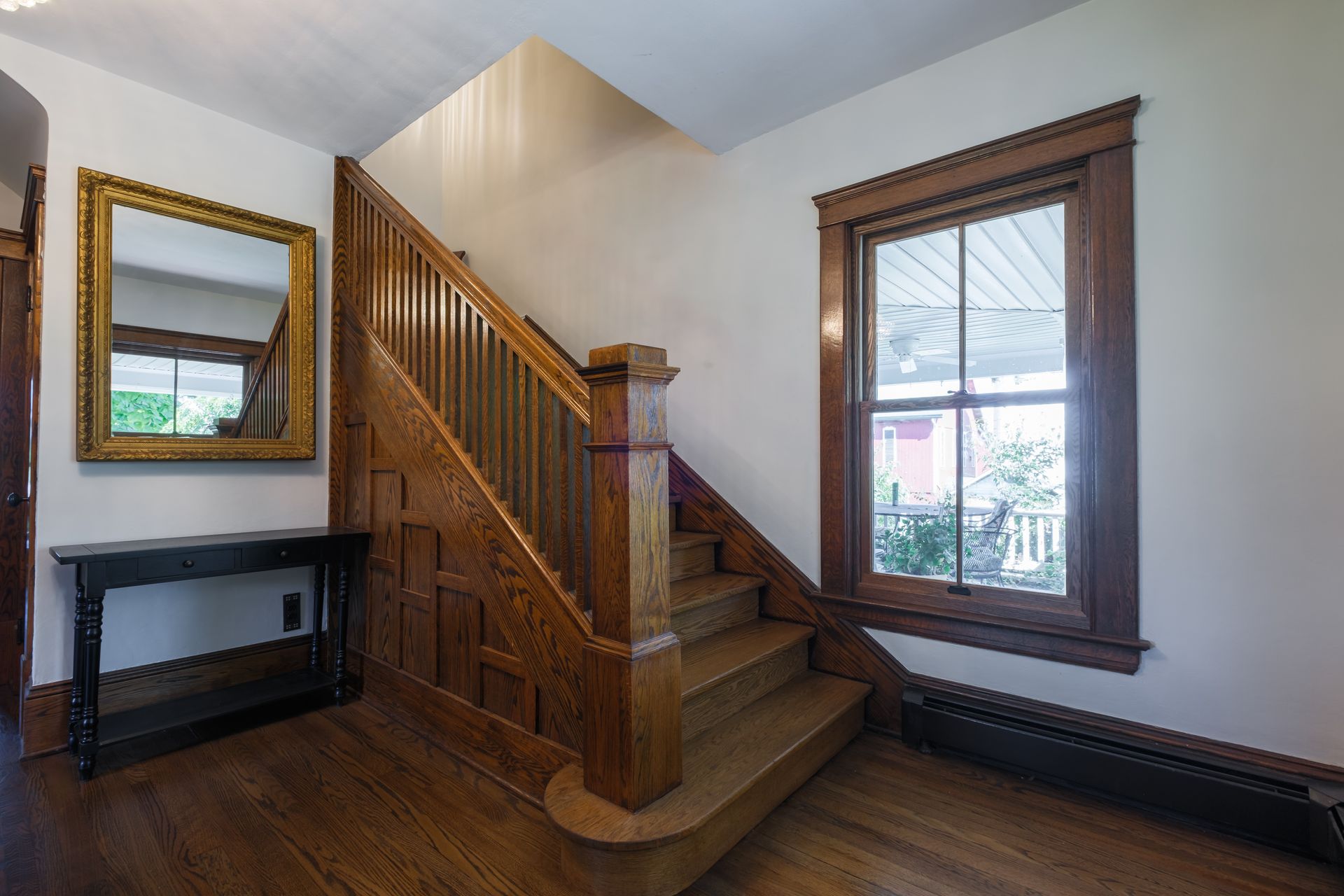 Wooden staircase and entryway with mirror and window.