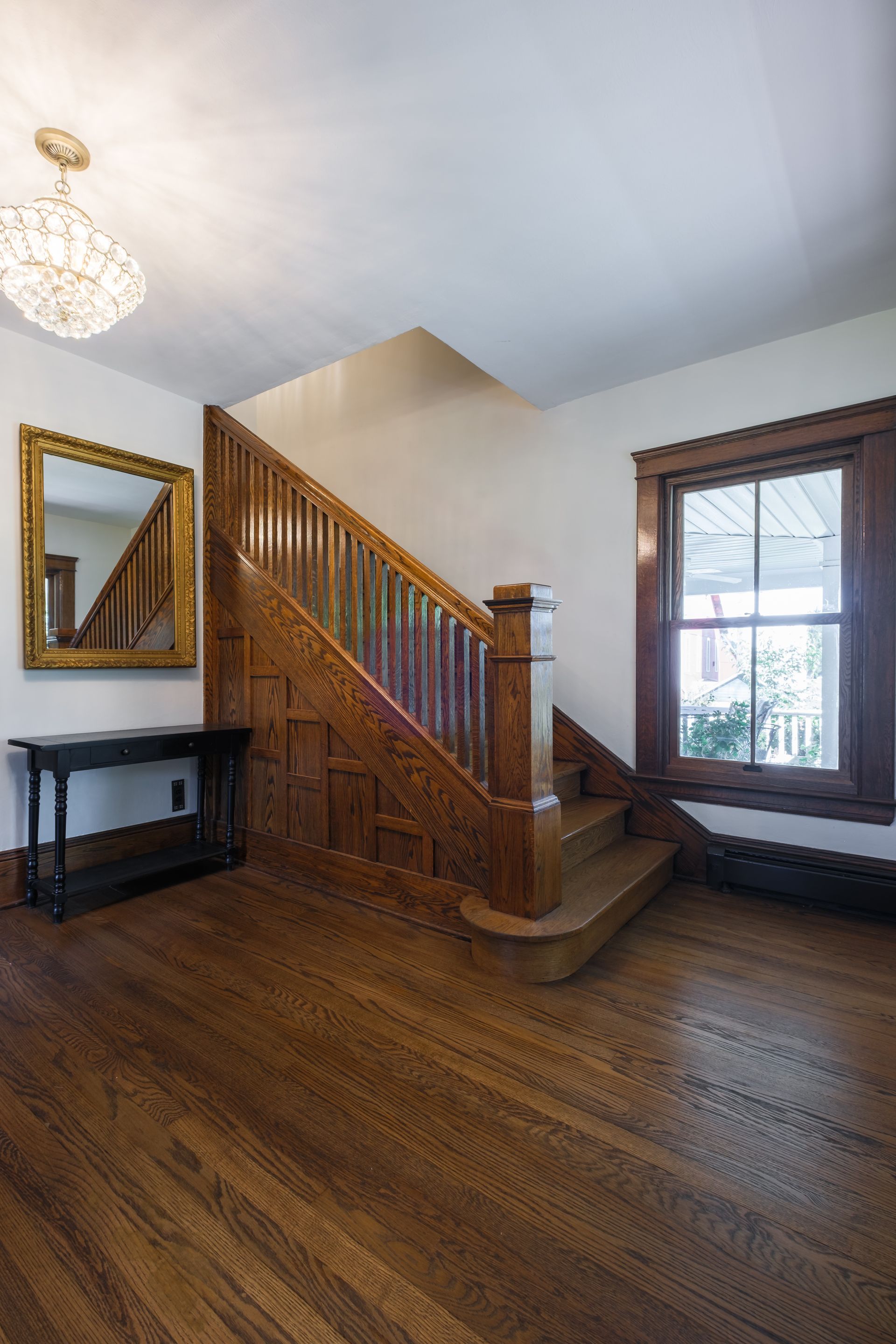 Wooden staircase in a home with hardwood floors, mirror, chandelier, and a window.