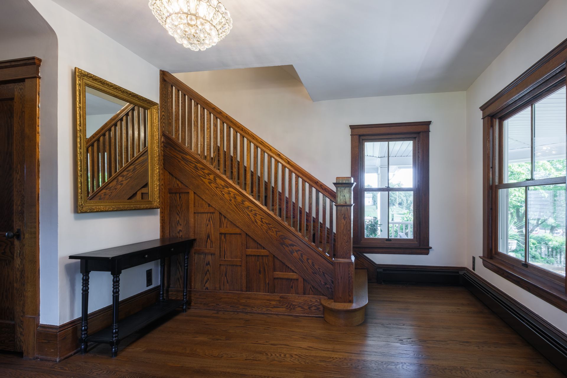 Wooden staircase in a home's entryway with a mirror, dark trim, and chandelier.