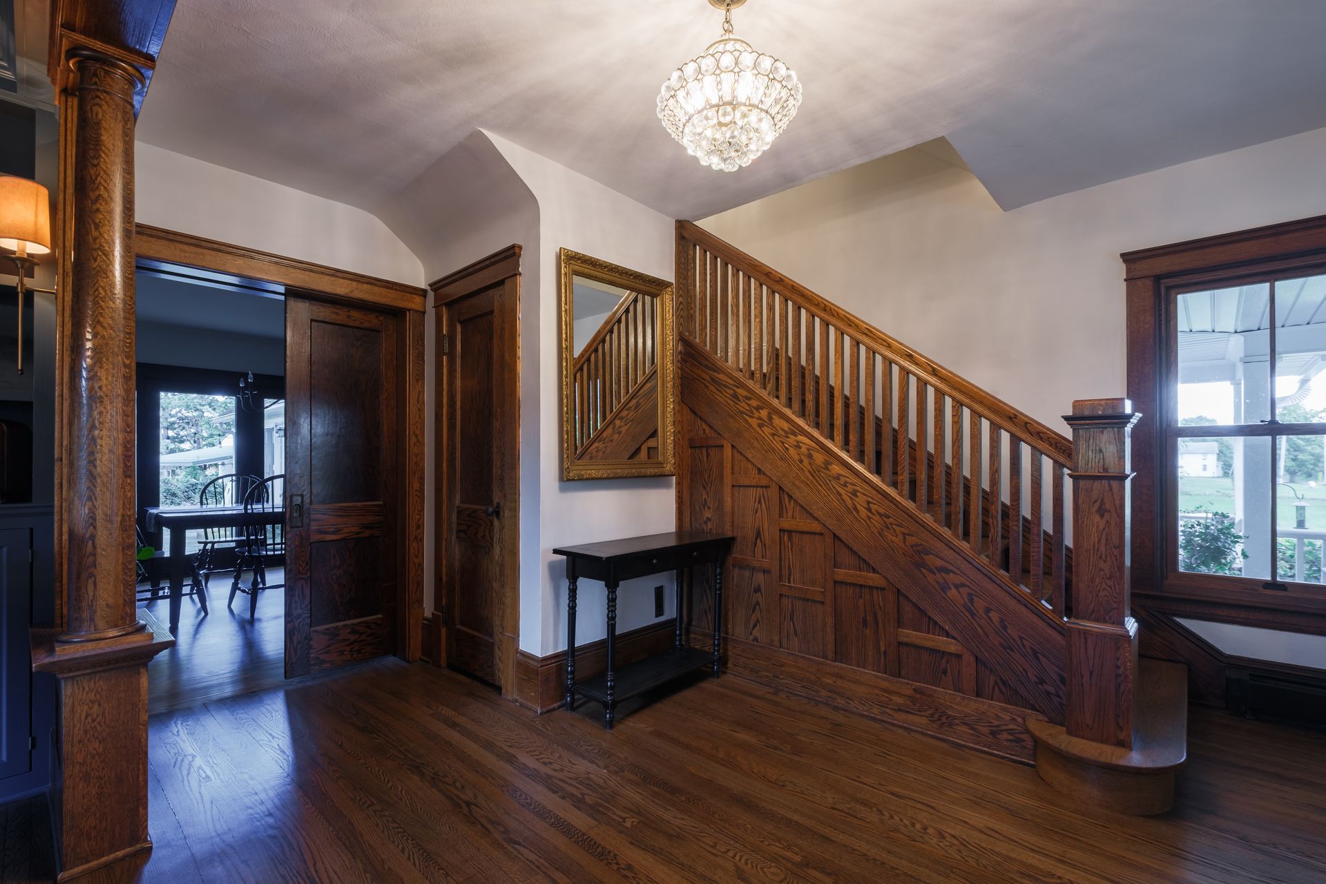 Wooden staircase in a home's entryway. Features include hardwood floors, a chandelier, and a decorative mirror.