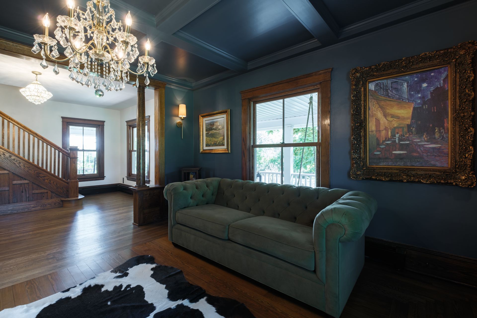 Elegant living room with blue walls, tufted green sofa, chandelier, and a cowhide rug.