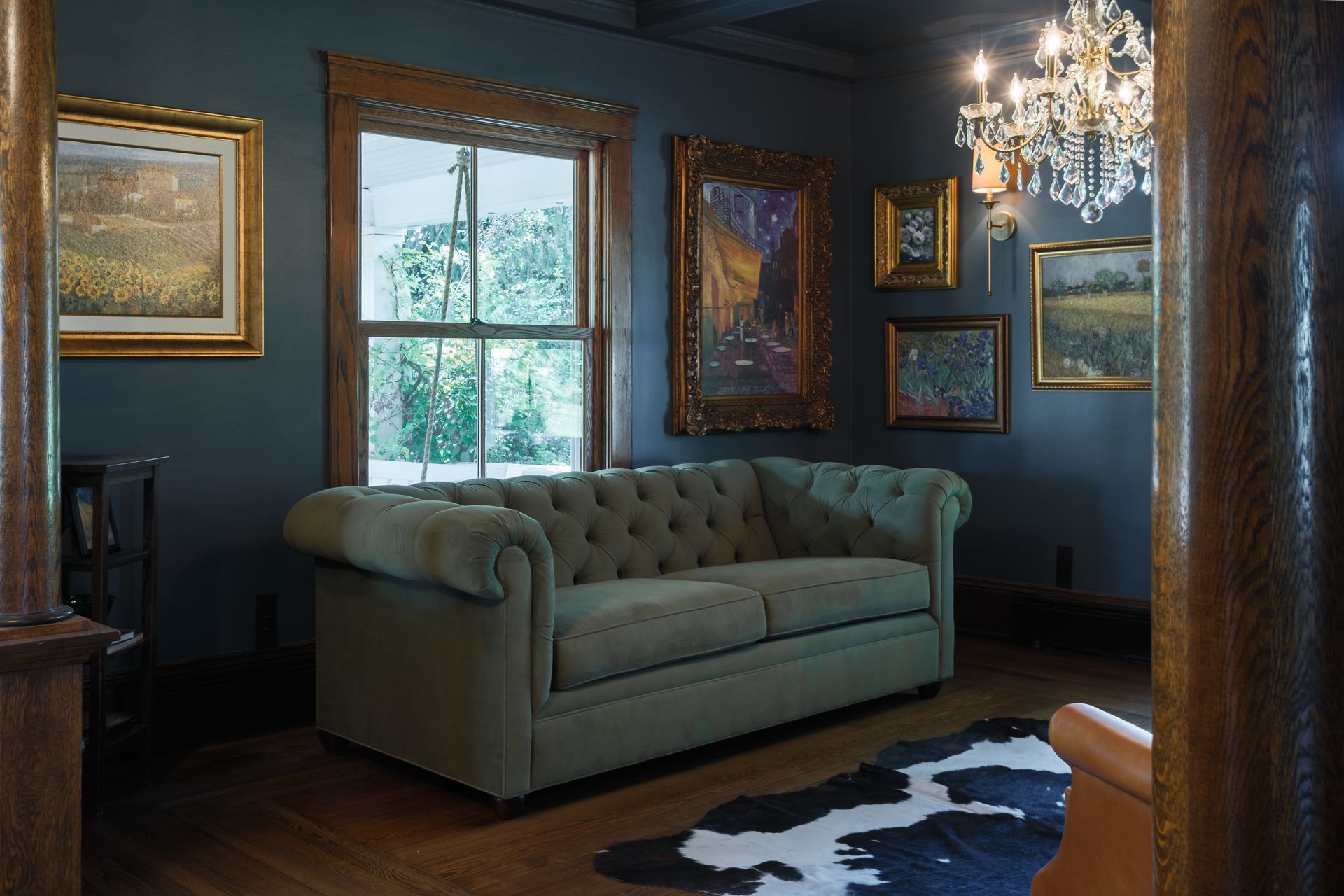 Green sofa in a dark room with artwork and a chandelier.