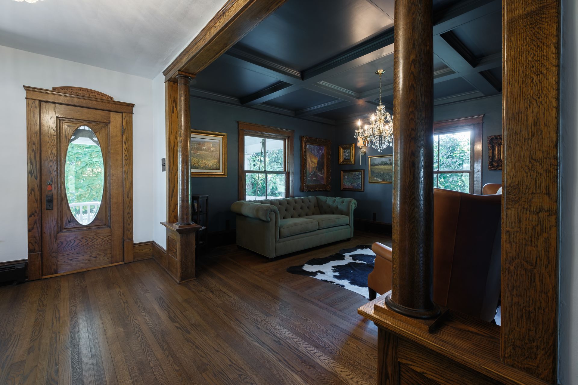 A hardwood-floored entryway with a wooden door, leading into a room with a sofa and dark blue walls.