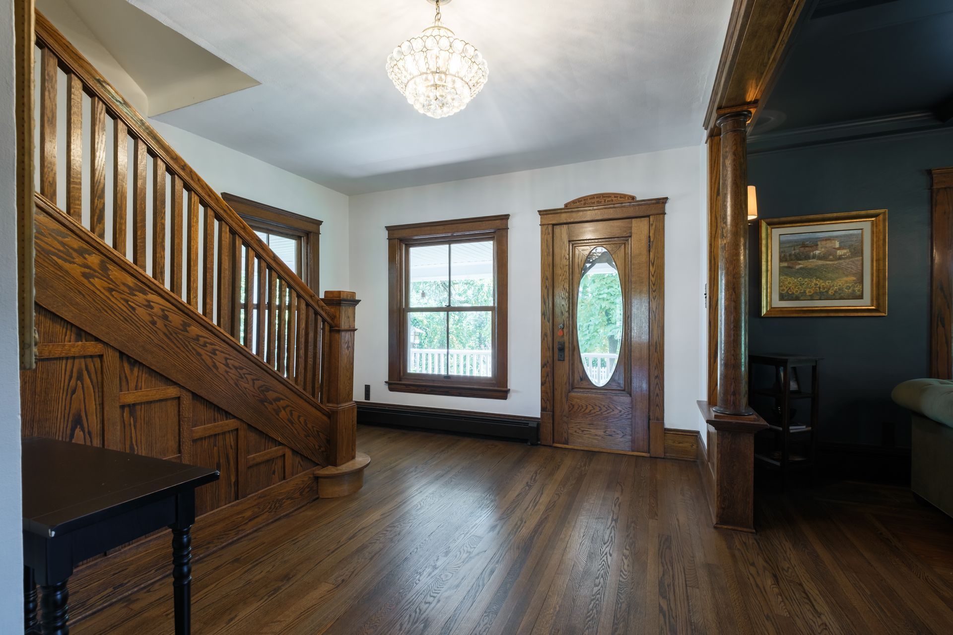 Wooden staircase and front door in an entryway with hardwood floors, a crystal chandelier, and a dark wall.