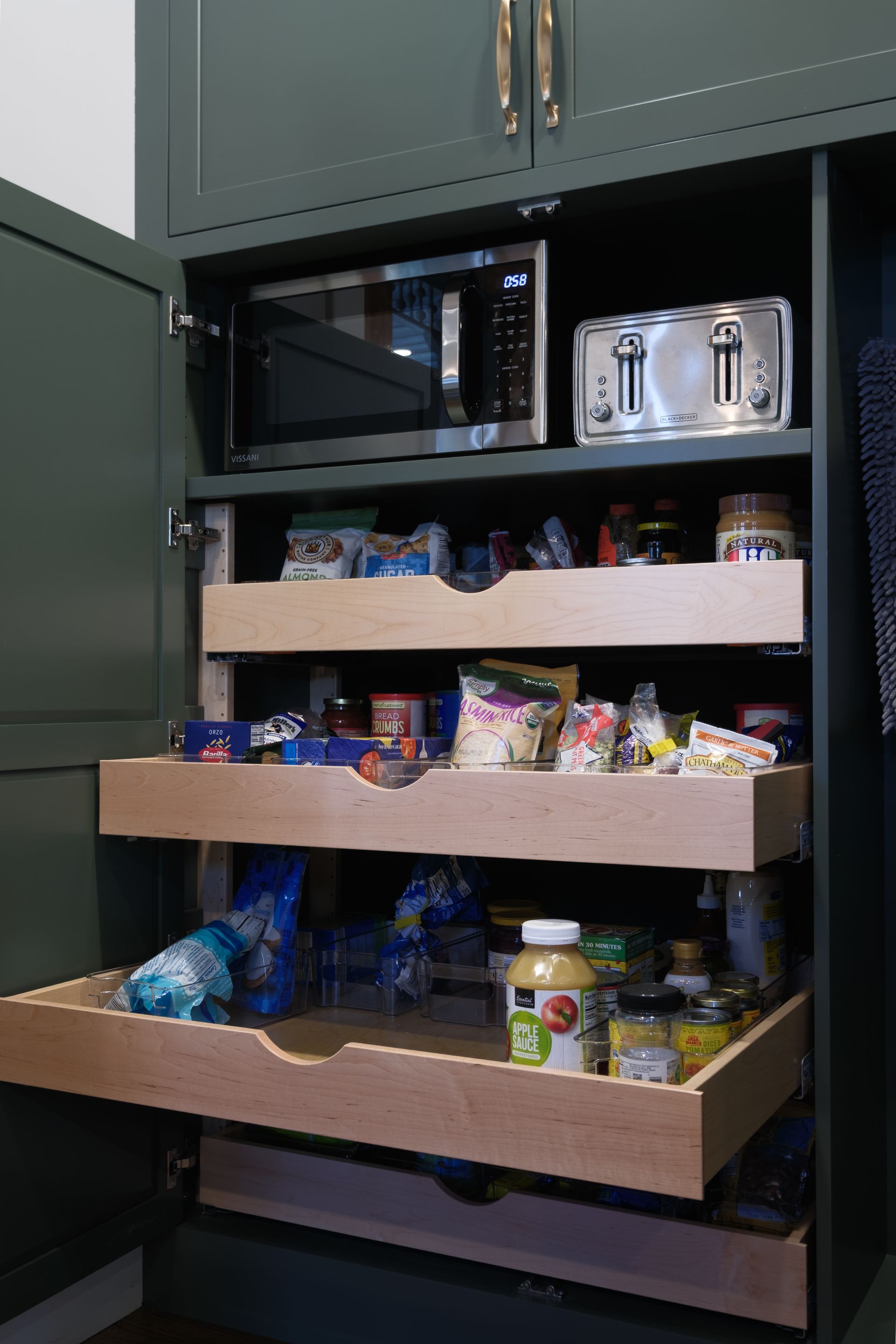 Dark green pantry with pull-out drawers, containing food items, a microwave, and a toaster.