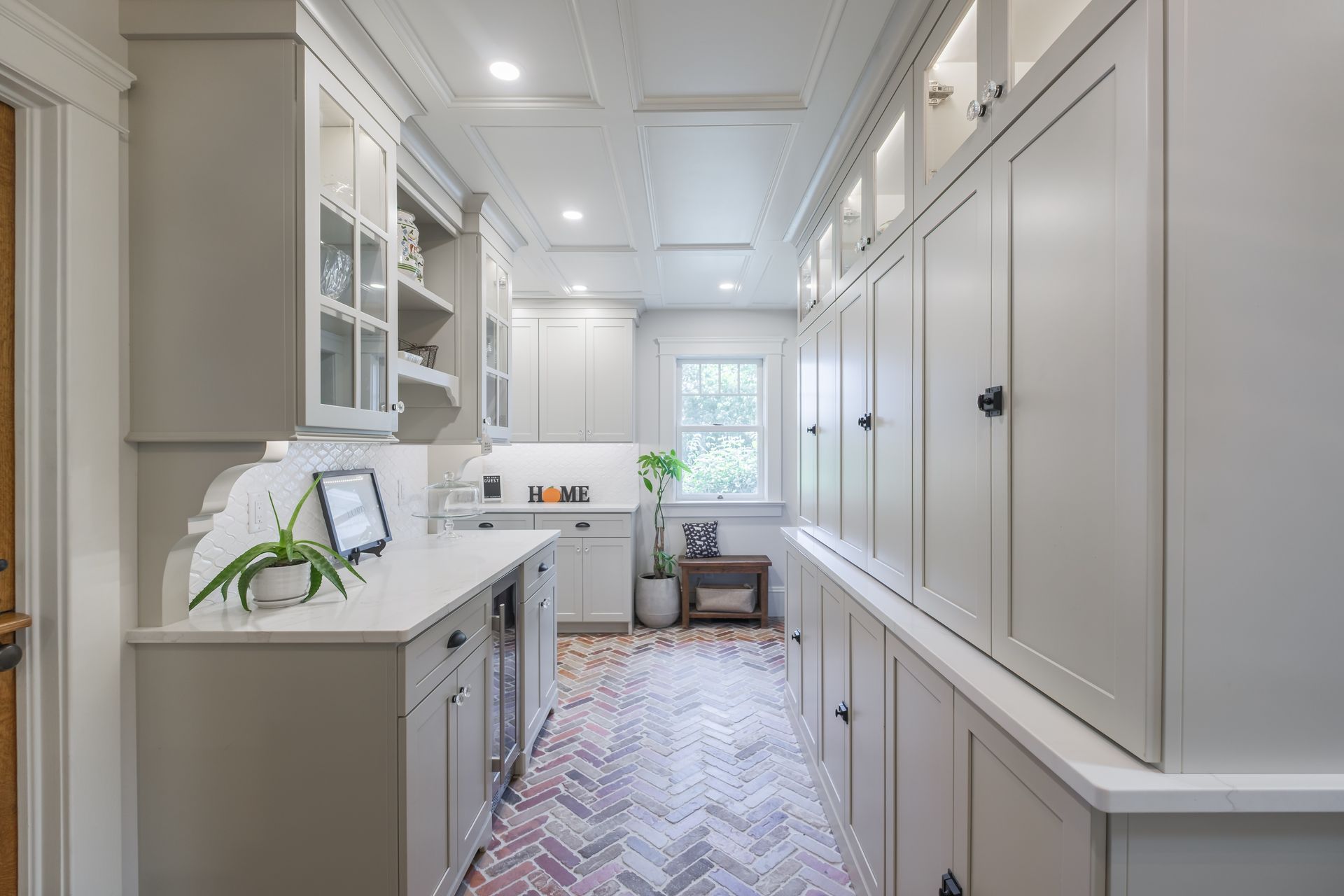 Narrow kitchen with gray cabinets, white countertops, and herringbone floor.