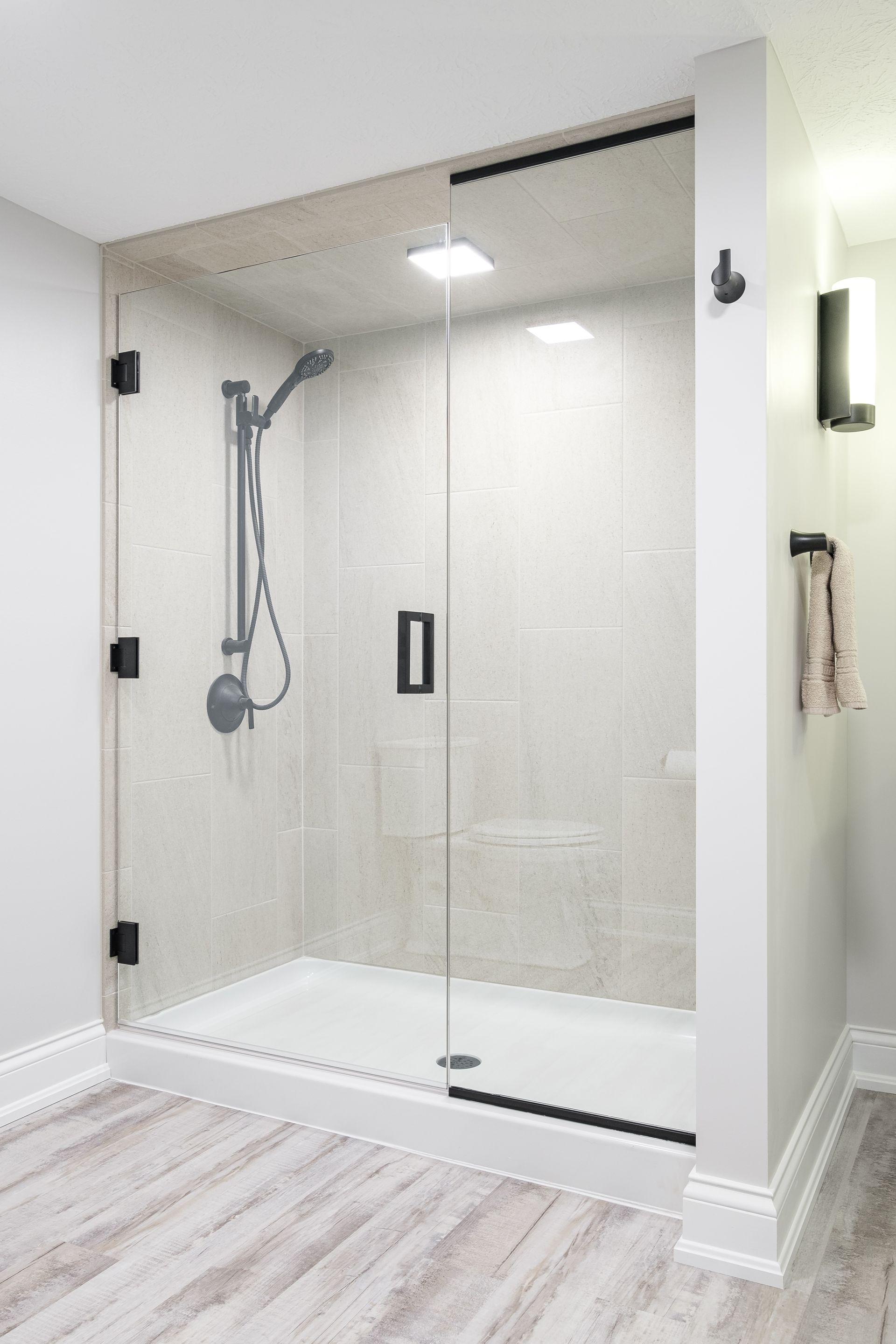 Glass shower enclosure with black hardware, white walls, and light gray flooring.