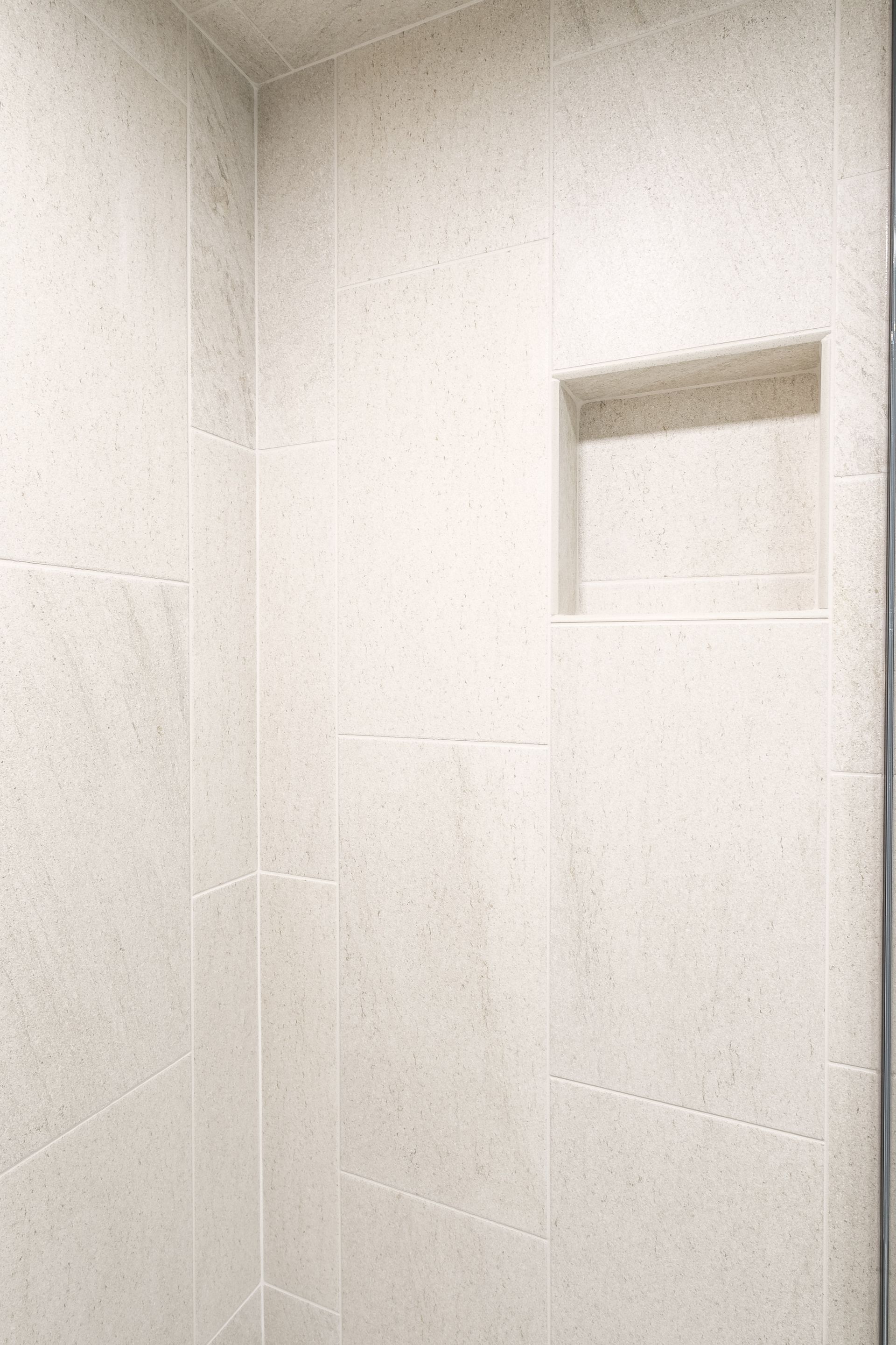 White tiled shower with built-in shelf.