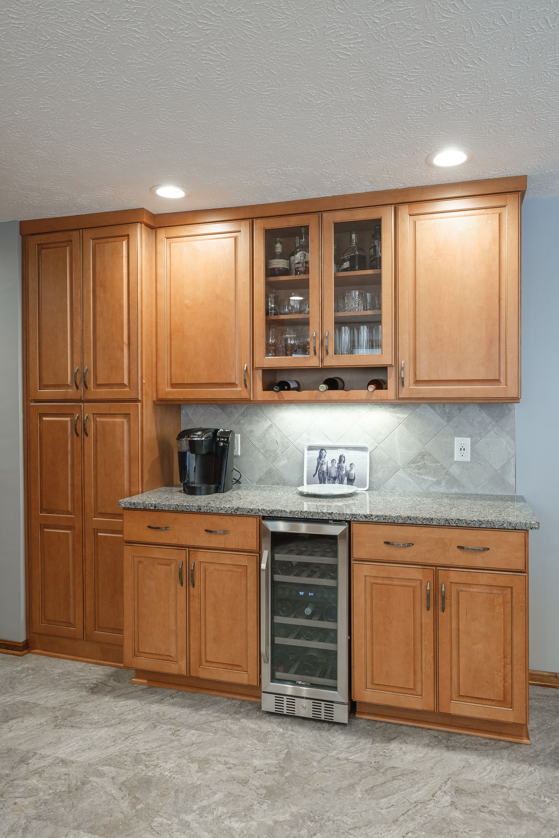 A kitchen with wooden cabinets , granite counter tops , and a wine cooler.