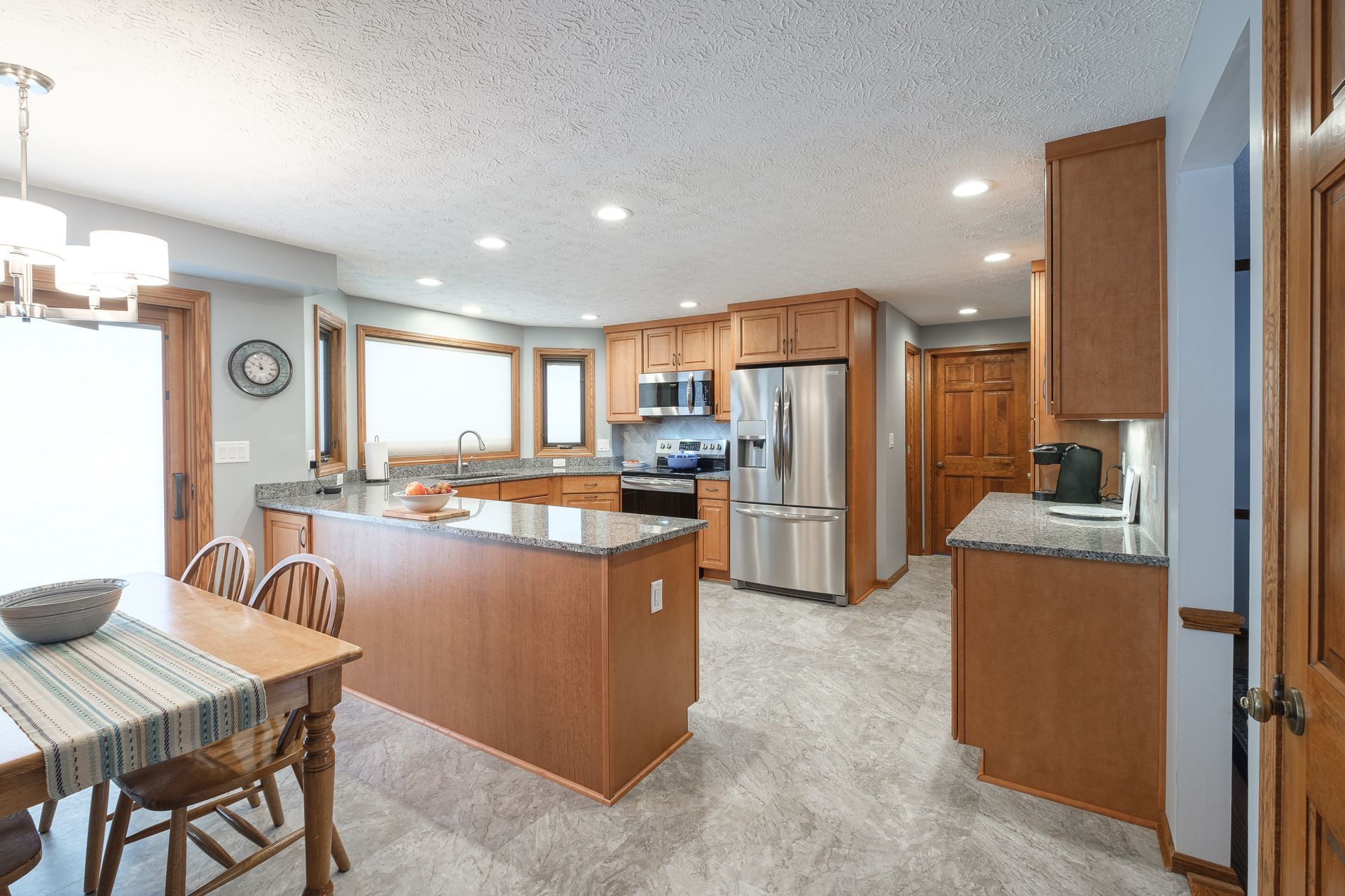 A kitchen with wooden cabinets , granite counter tops , stainless steel appliances , a table and chairs.