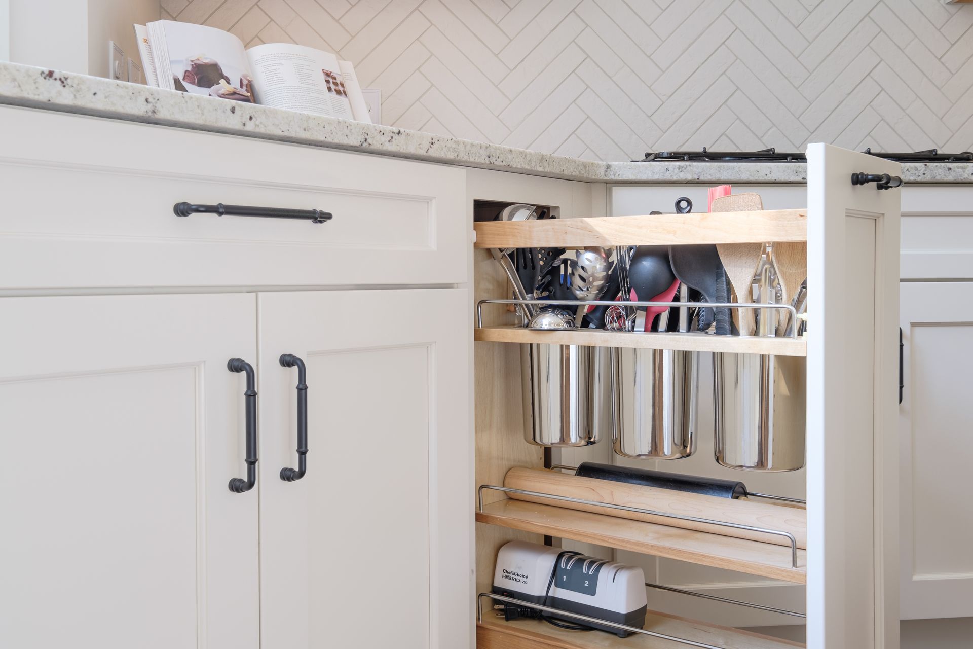 A kitchen with white cabinets and a pull out drawer filled with pots and pans.