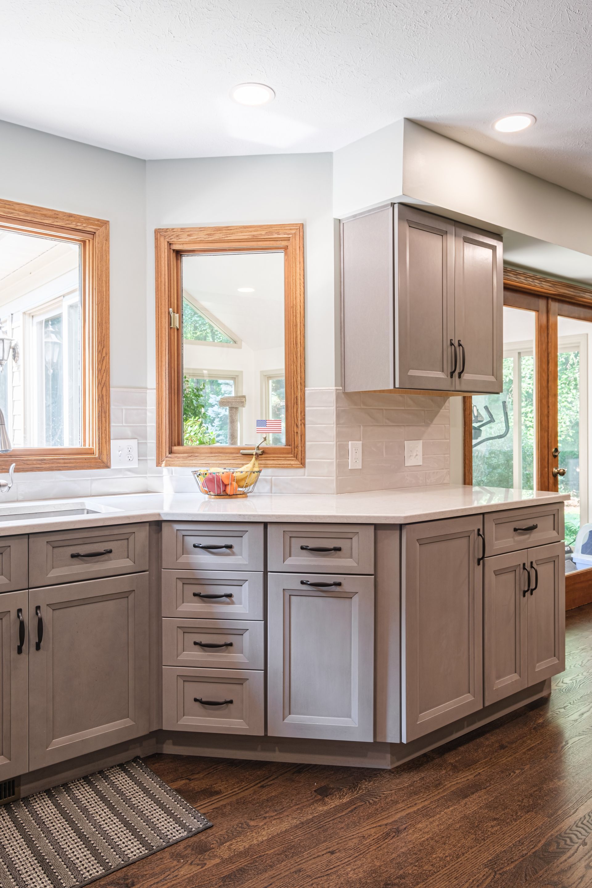A kitchen with gray cabinets , white counter tops , a sink and a mirror.
