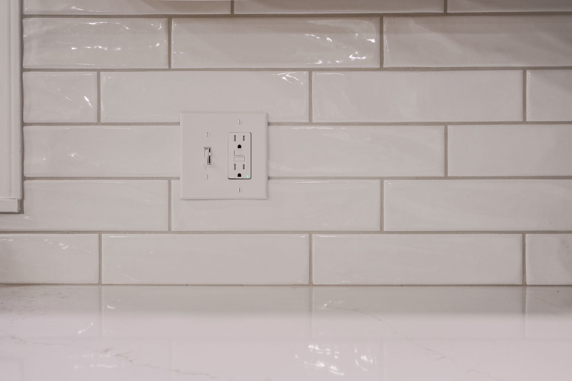 A white subway tile wall with a white electrical outlet.