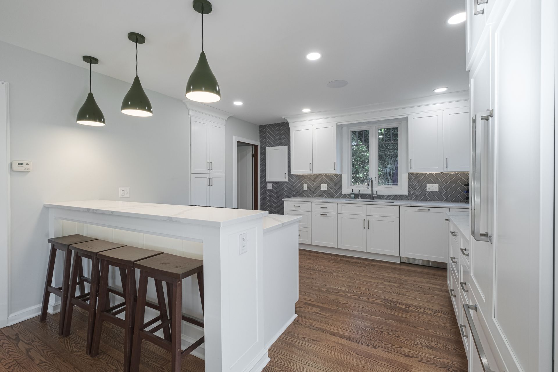 A kitchen with white cabinets , wooden floors , and stools.