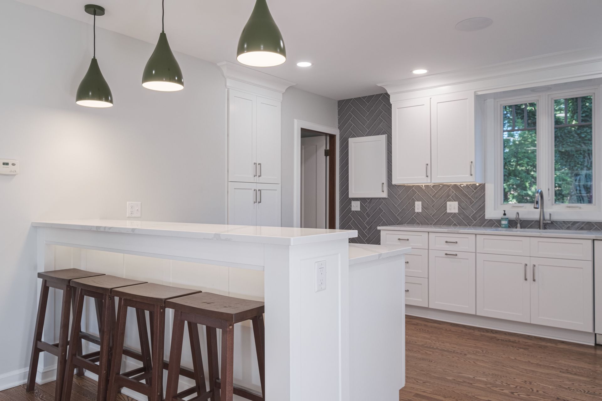 A kitchen with white cabinets , wooden floors and stools.