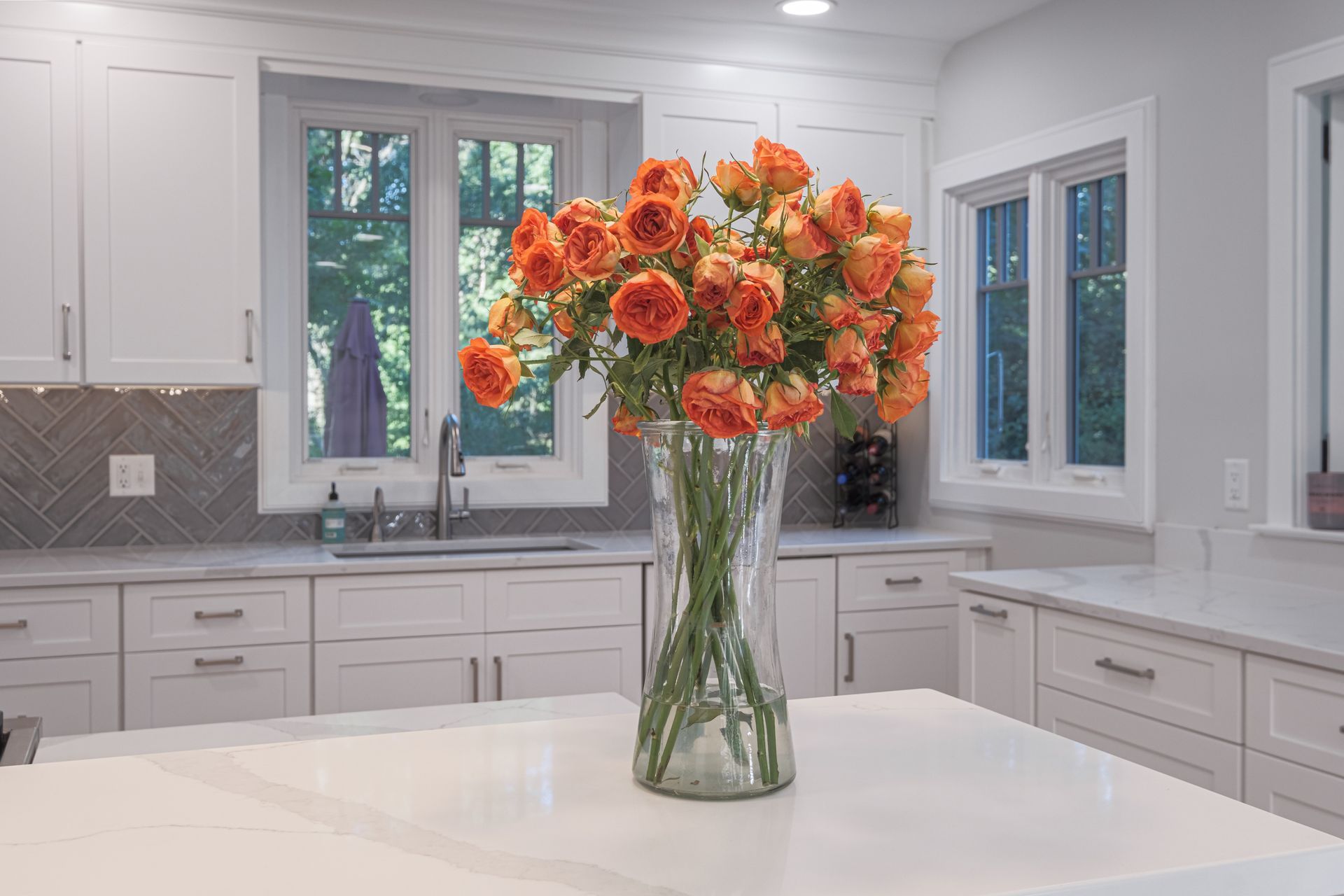 A vase of orange roses is sitting on a kitchen counter.
