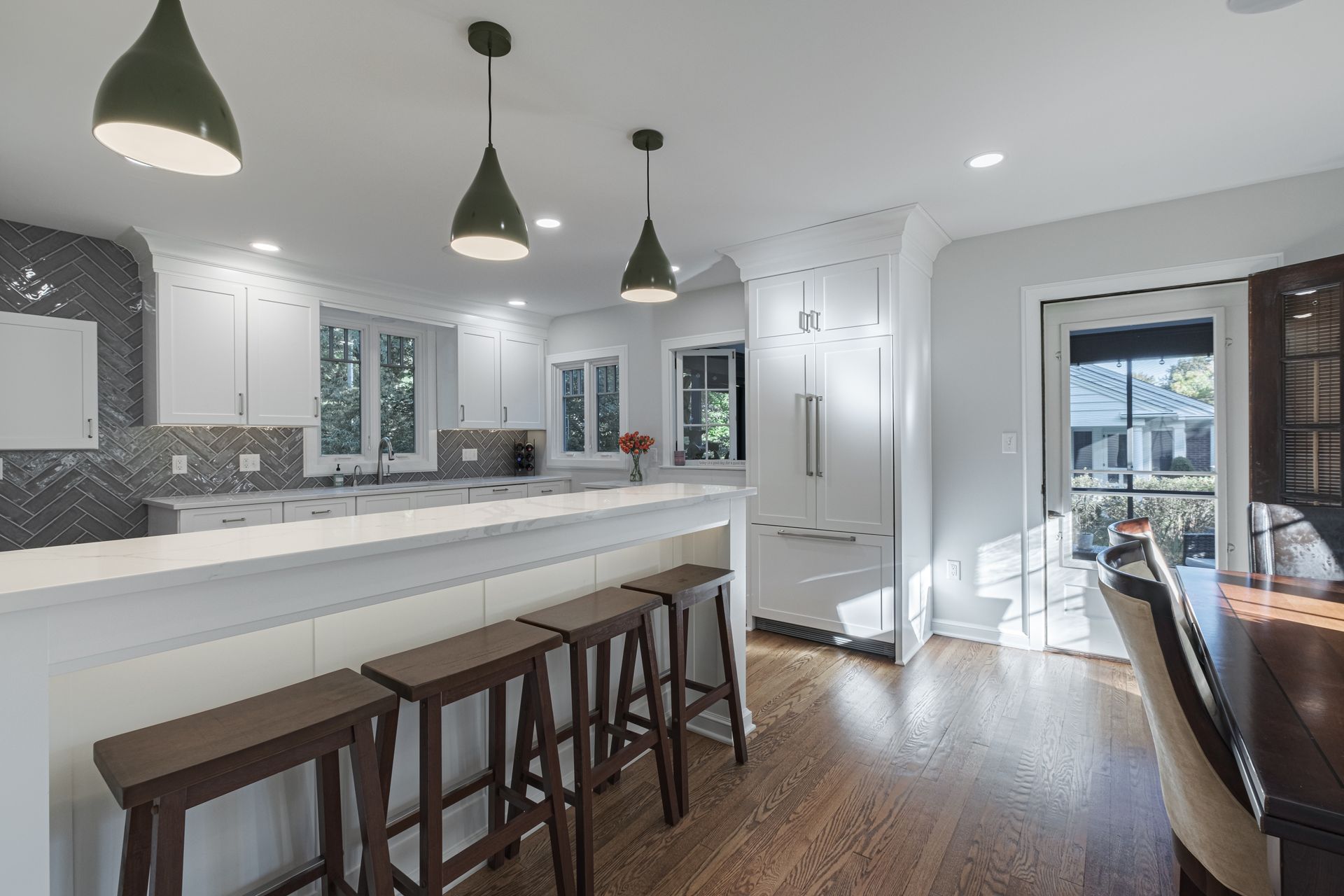 A kitchen with a long island , stools , a table and a refrigerator.