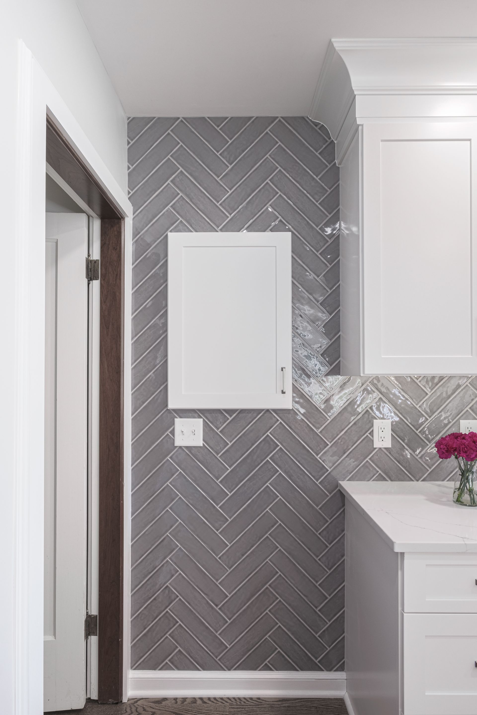 A laundry room with gray herringbone tiles and white cabinets.
