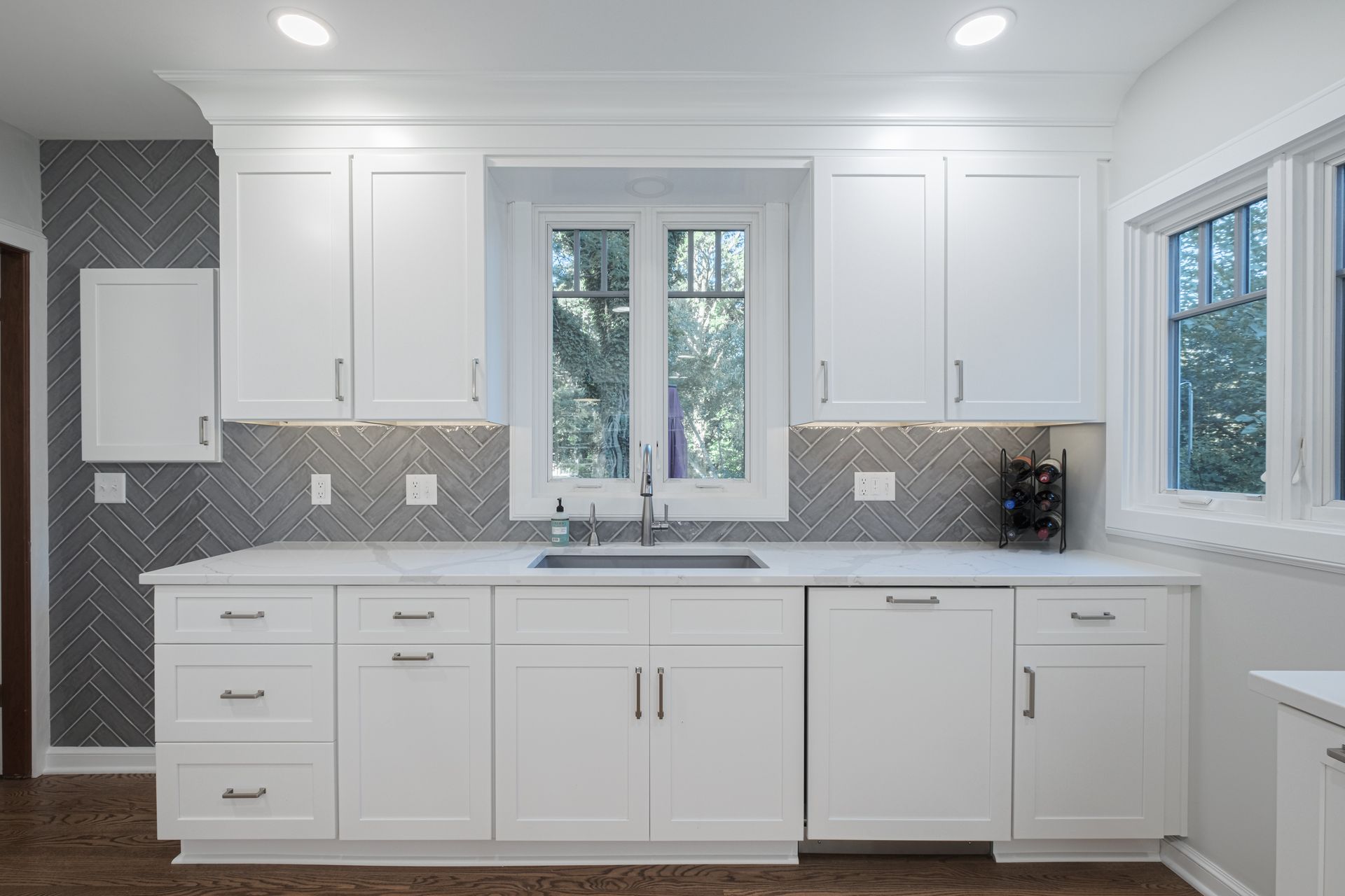 A kitchen with white cabinets , a sink , and a window.