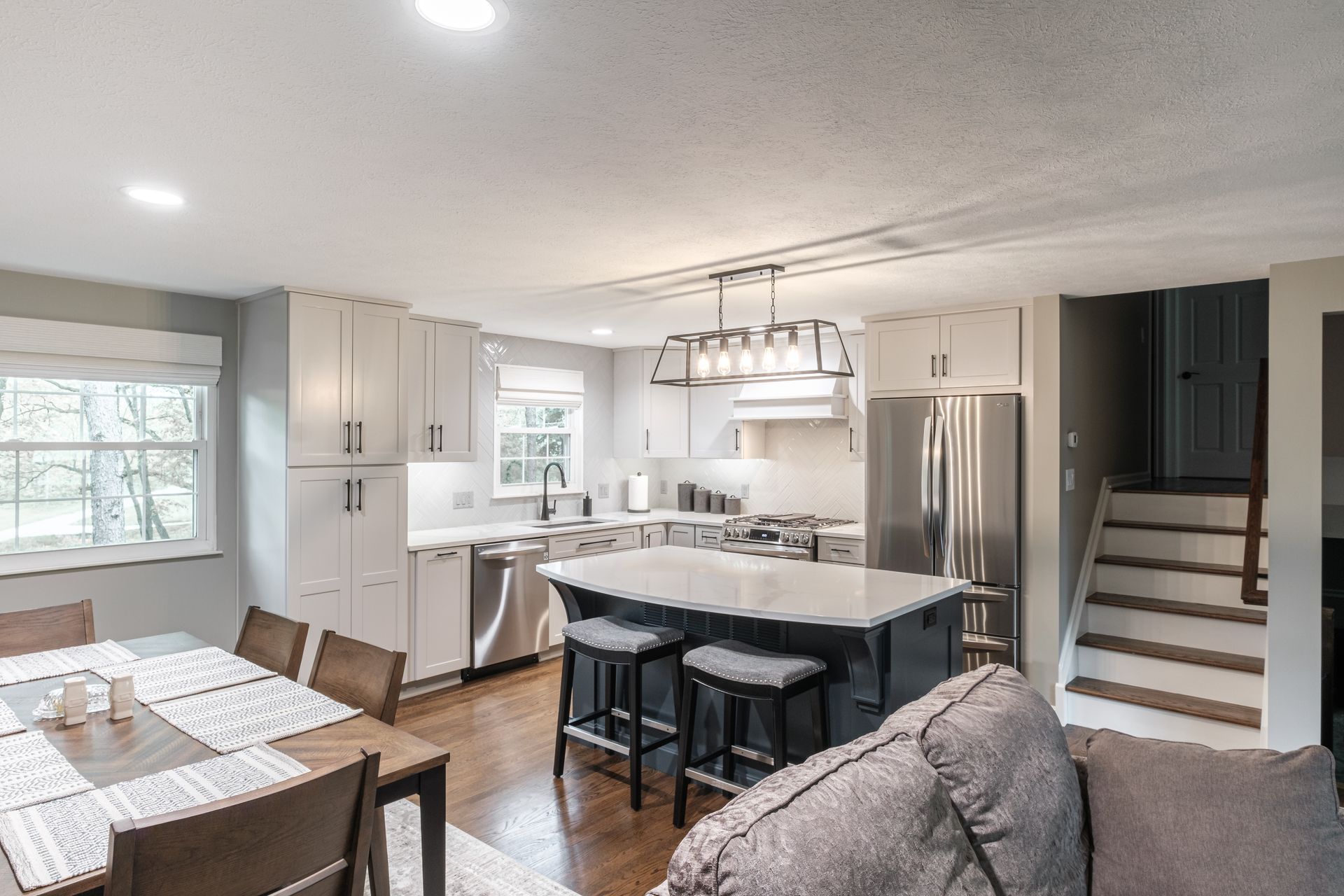 A kitchen with white cabinets , stainless steel appliances , a large island , a table and chairs.
