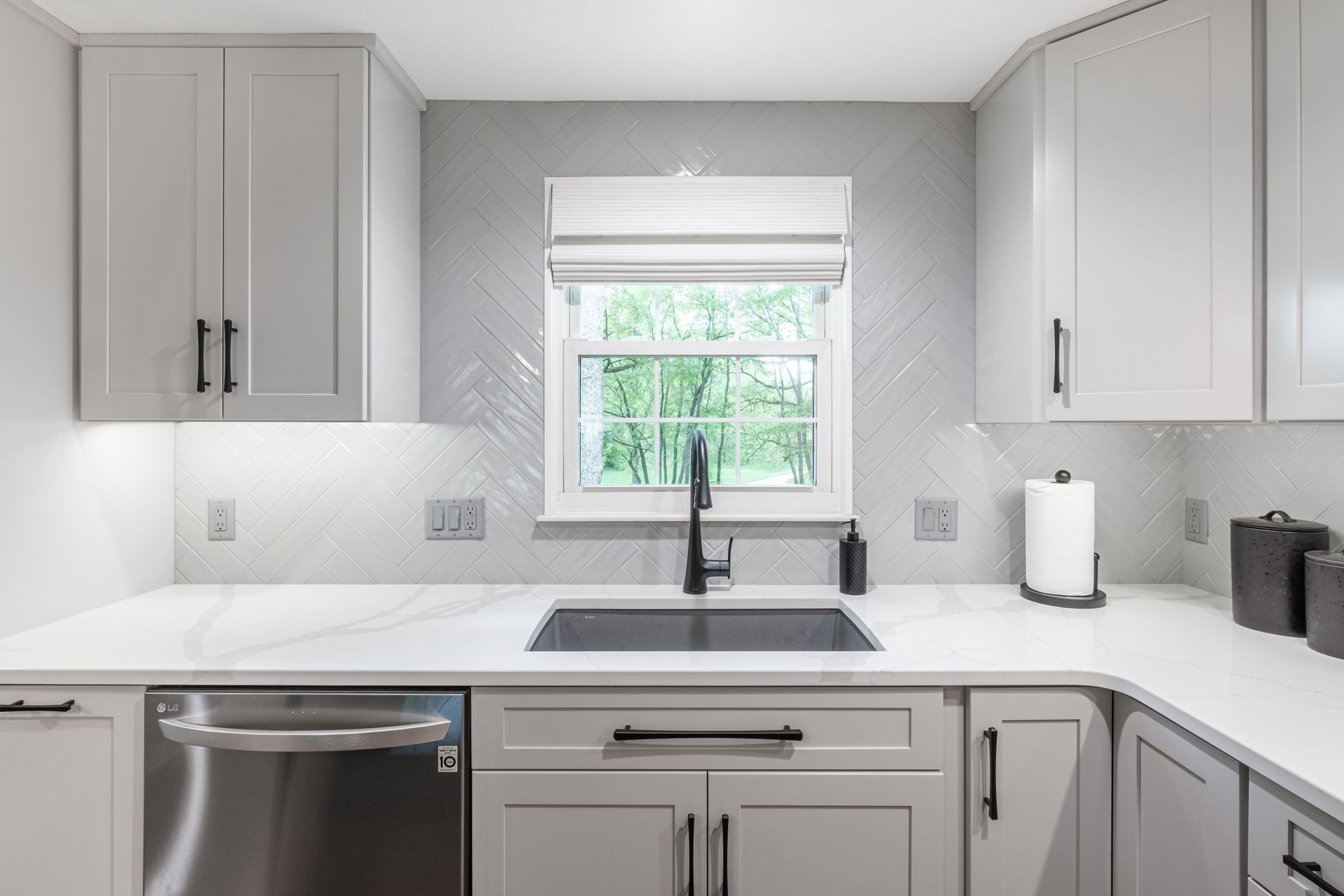 A kitchen with white cabinets , a sink , a dishwasher , and a window.
