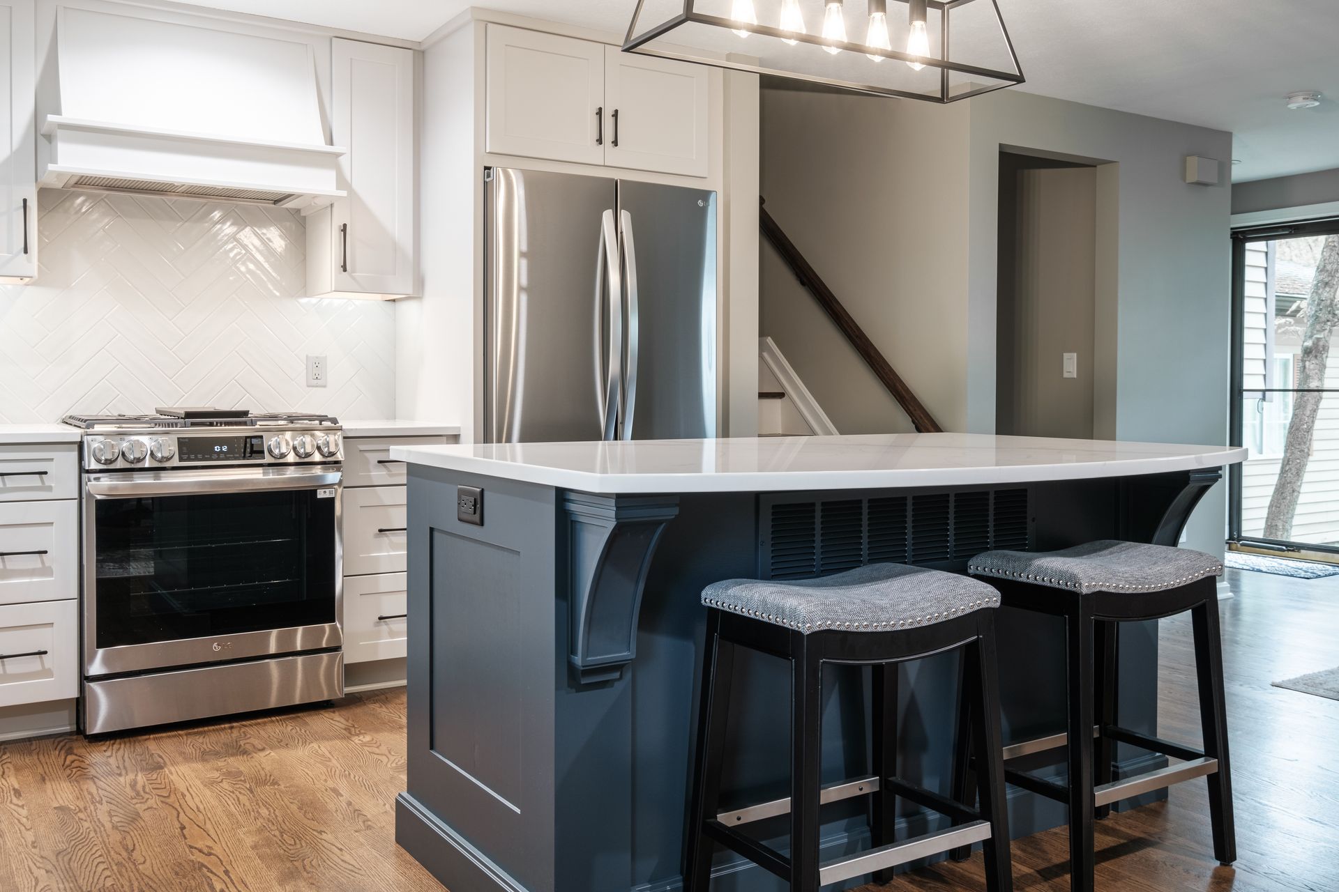 A kitchen with a large island , stools , a refrigerator and a stove.