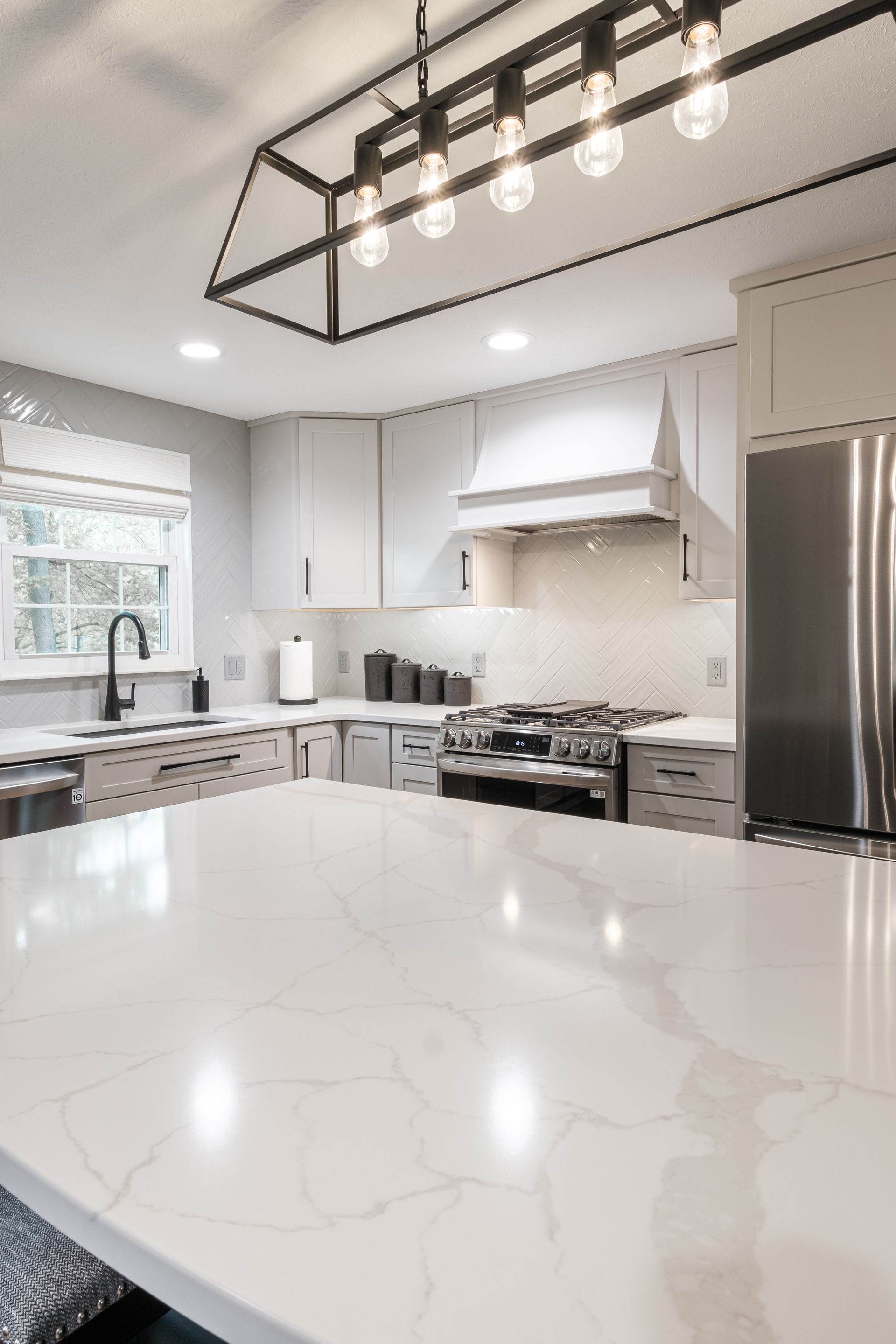 A kitchen with white counter tops , stainless steel appliances , and a large island.