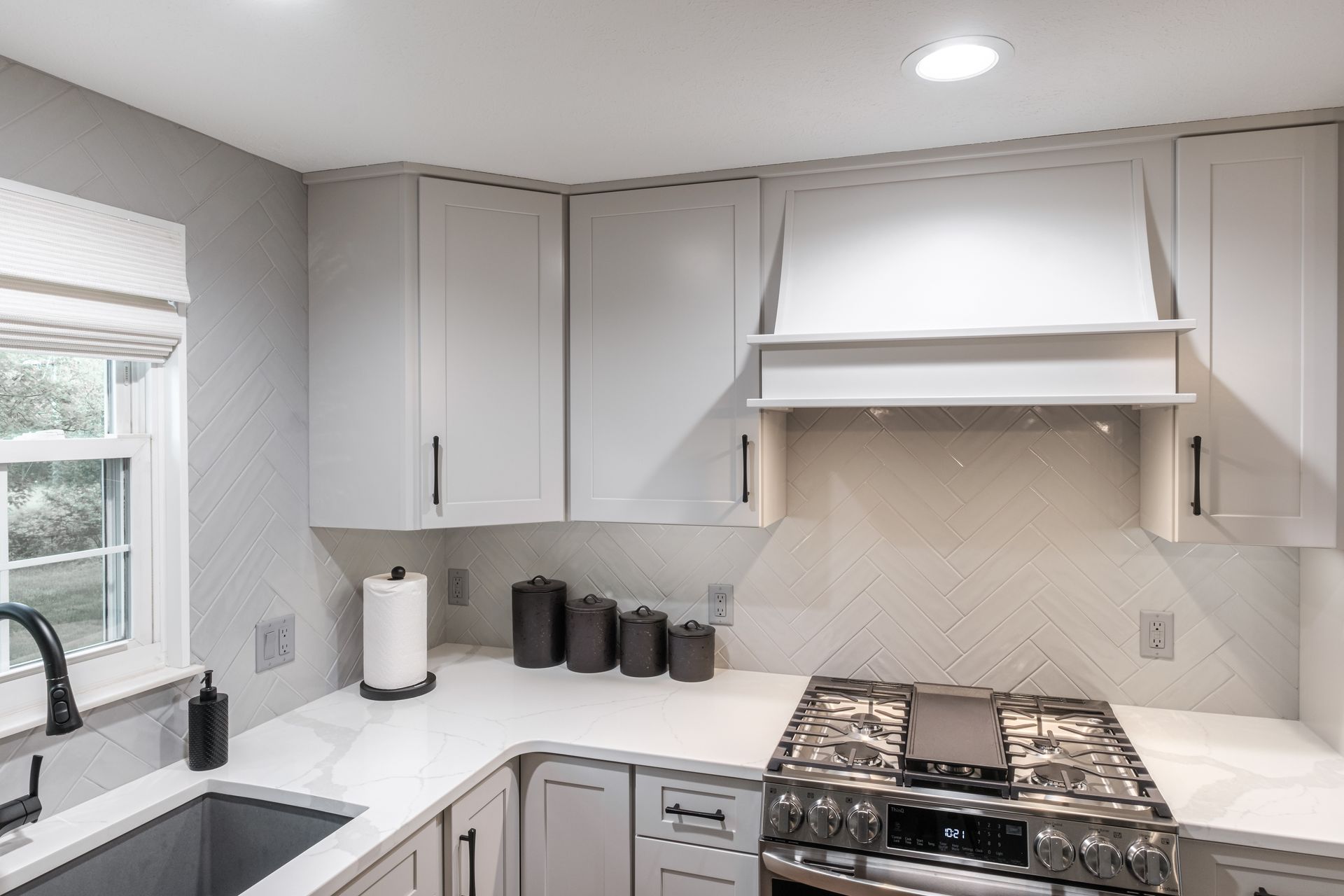 A kitchen with white cabinets , a stove , a sink , and a window.