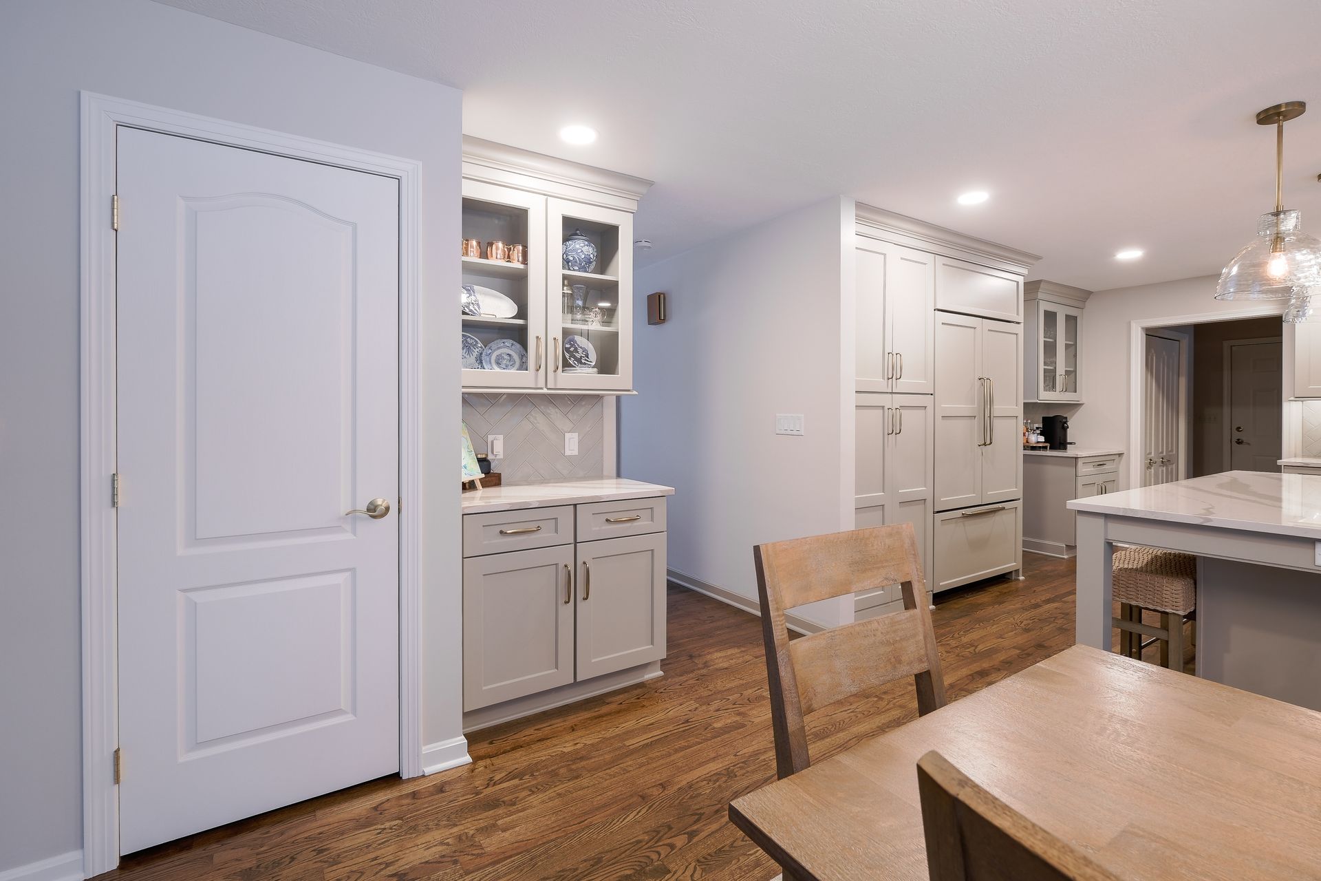 Kitchen with cabinets, fridge, and door. Wooden floor and table; neutral color scheme.