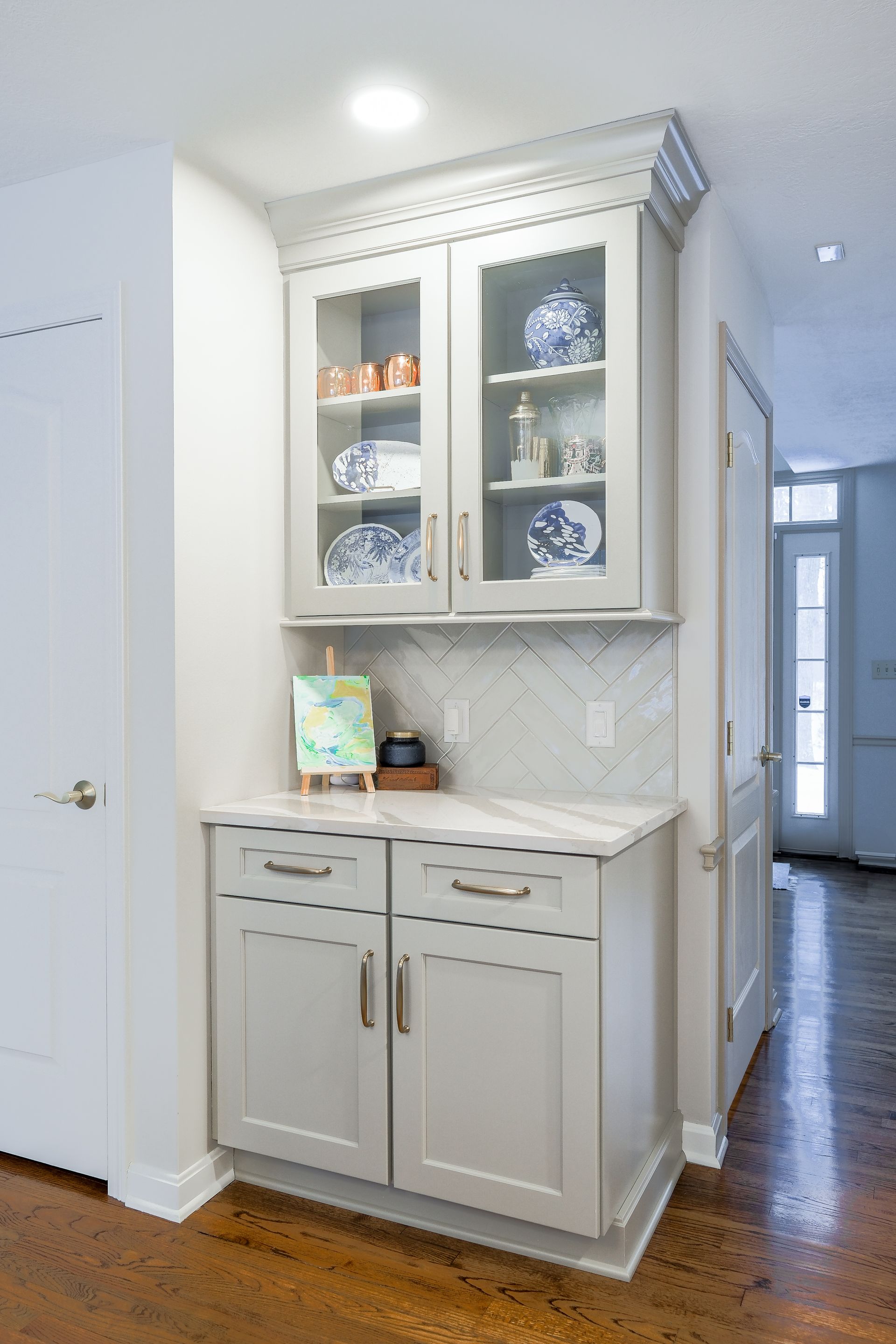 Gray built-in cabinet with glass doors displaying plates and decor, situated in a hallway.
