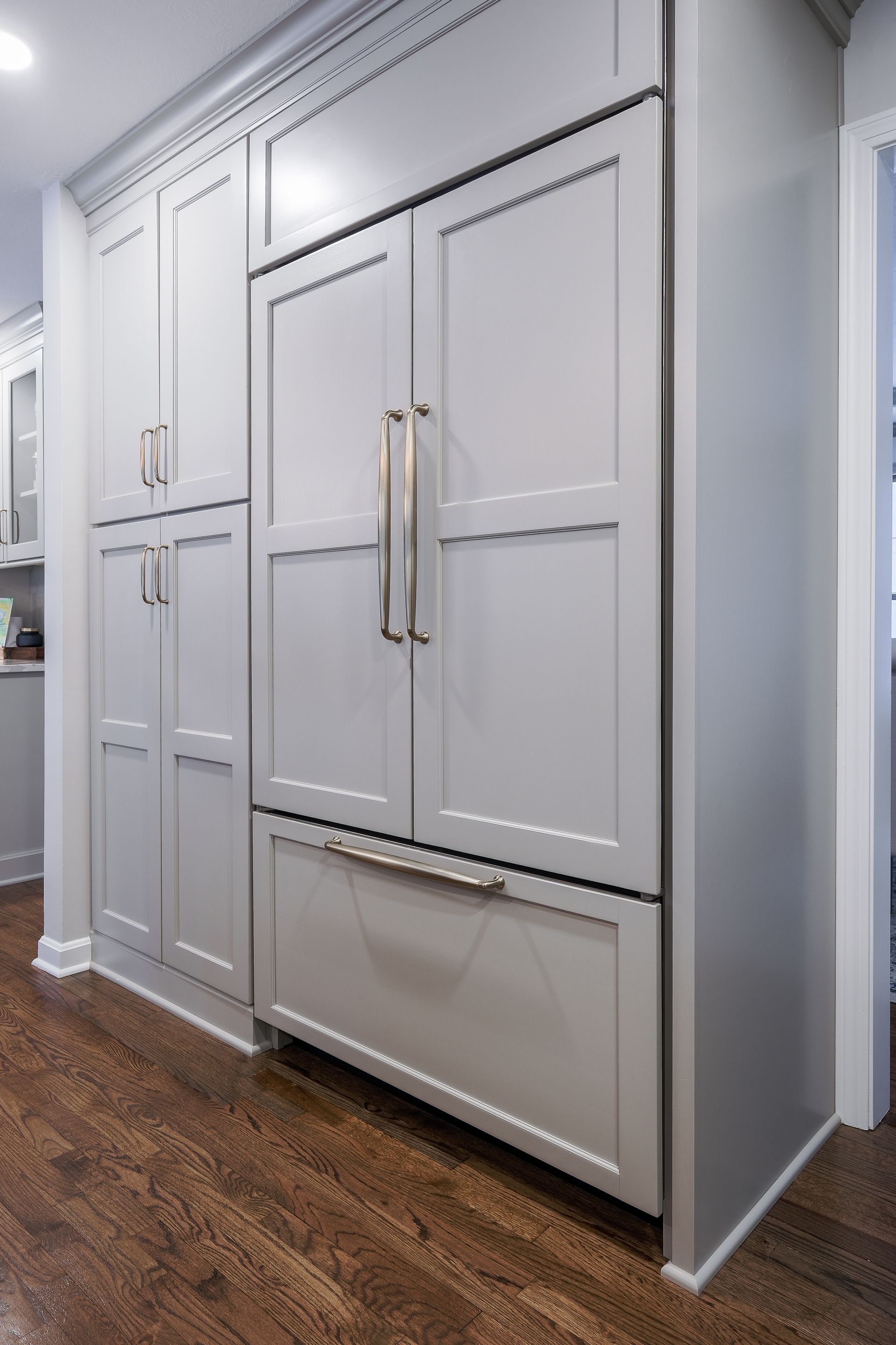 Gray built-in refrigerator and cabinetry with stainless steel handles in a kitchen with wood floors.